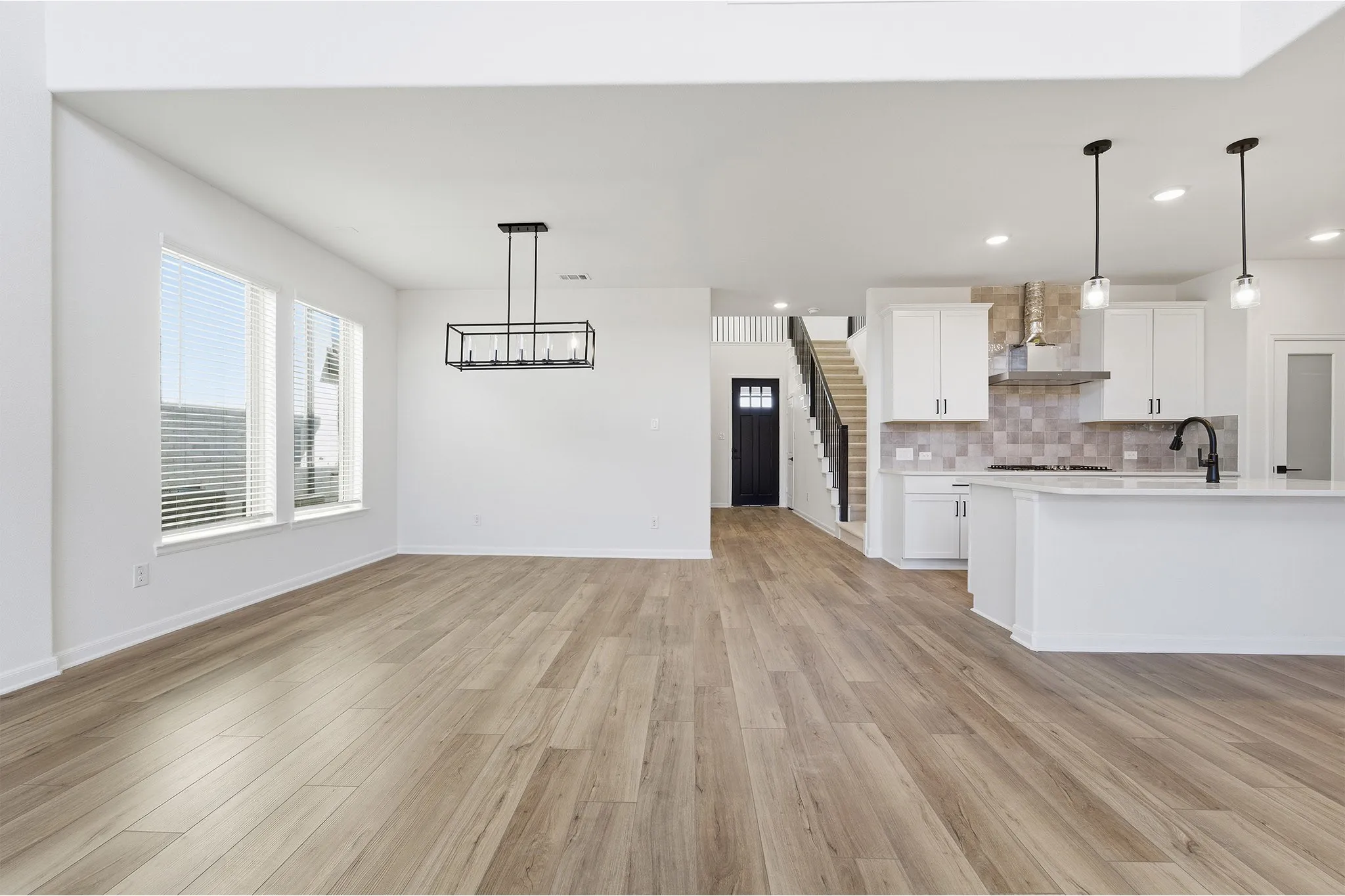 Open-concept living space with wood-finish flooring, white walls, and a modern linear chandelier