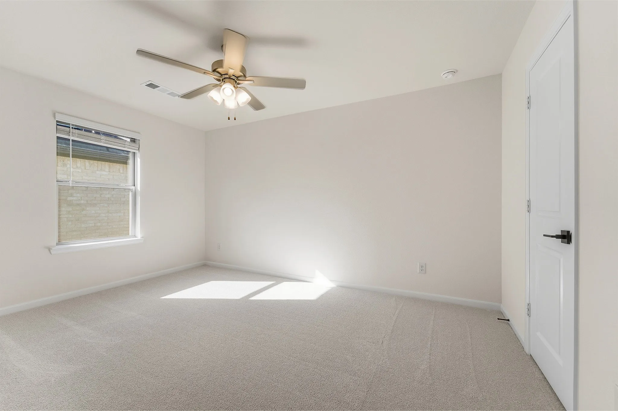 Carpeted room featuring a ceiling fan with integrated lighting, a single window with blinds, and a white paneled door with a black handle