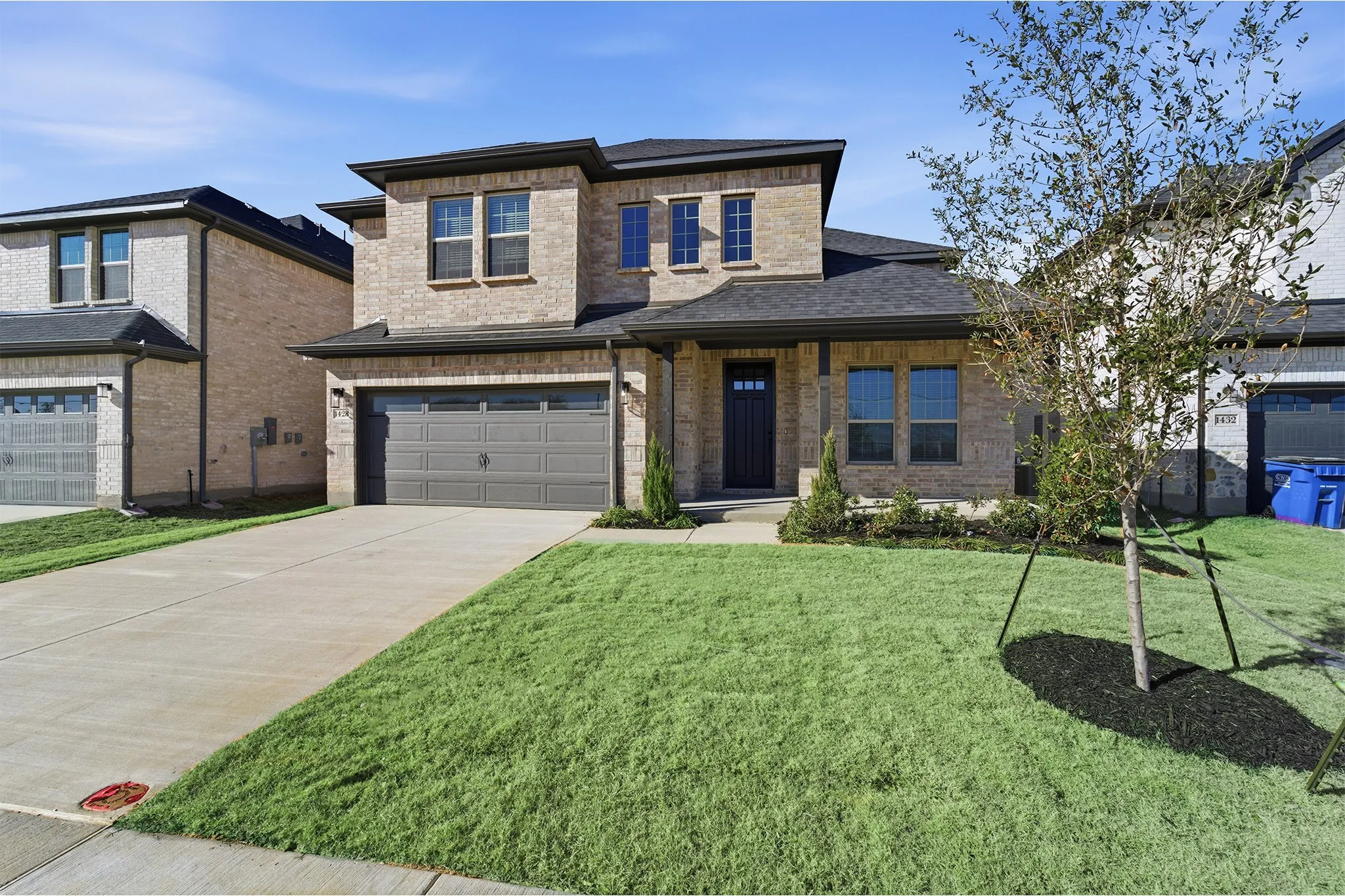 Brick facade, two-car garage, covered entry, and front landscaping