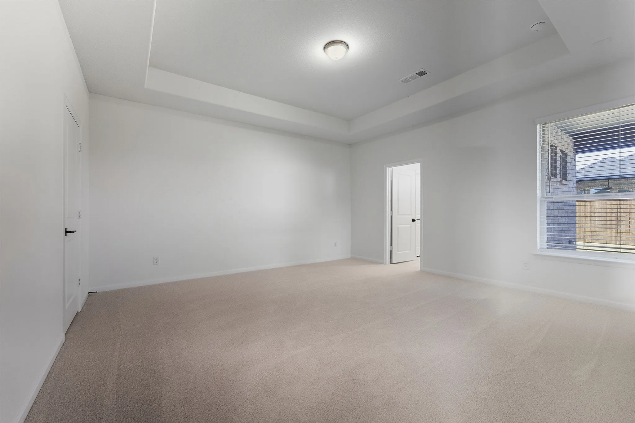 Spacious room with tray ceiling, neutral-toned carpeting, and white walls