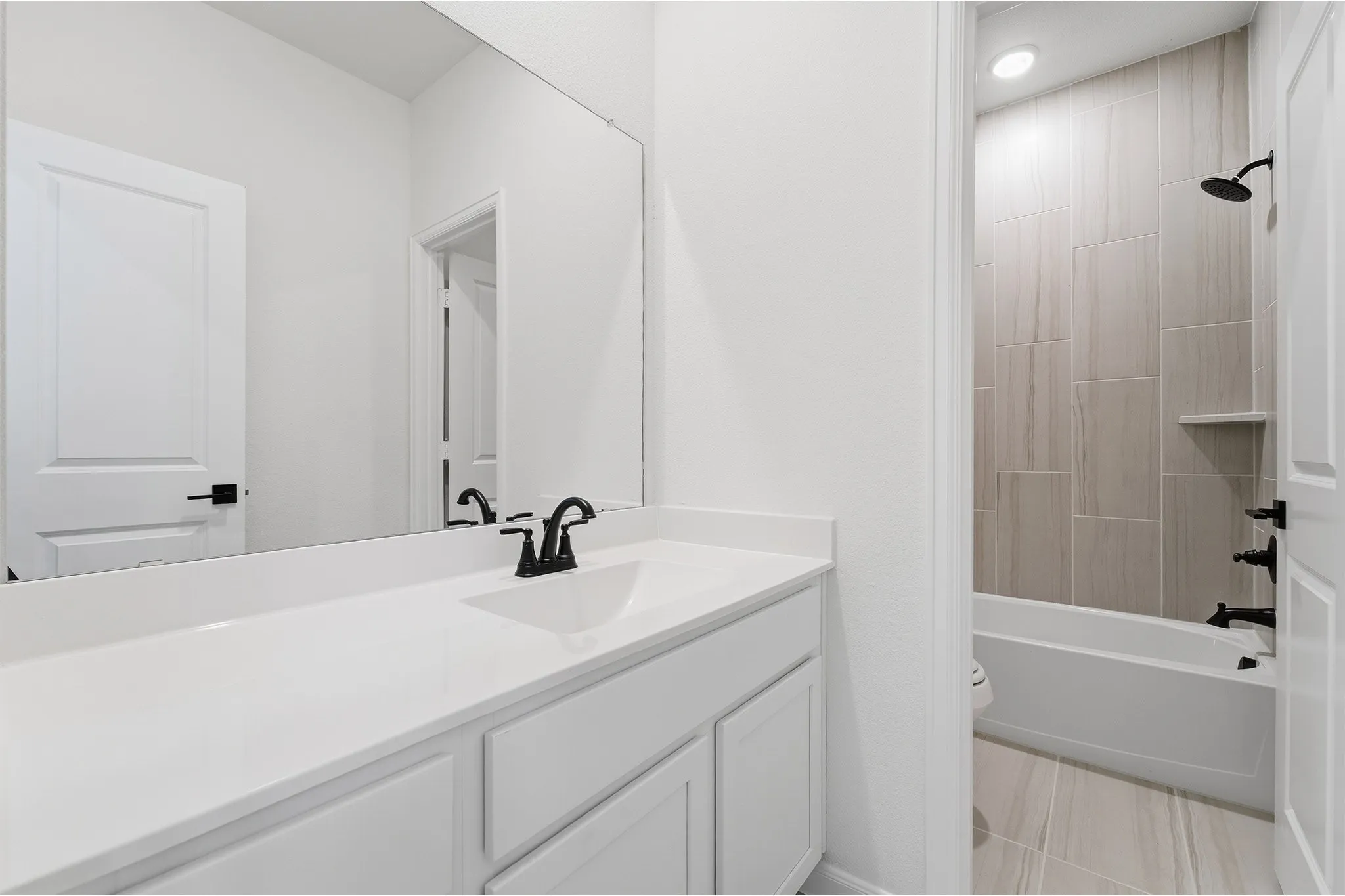 Bathroom featuring a white vanity with an integrated sink, black faucet, and a large wall-mounted mirror