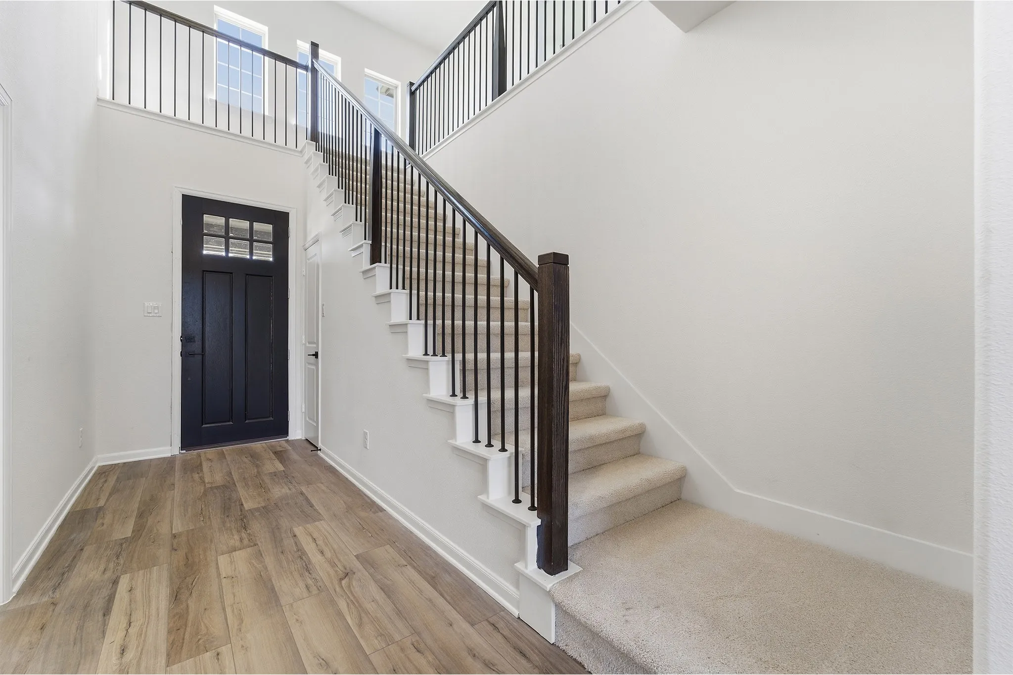 Two-story foyer featuring wood-finish flooring, a contemporary staircase with dark wood newel posts, and wrought iron balusters