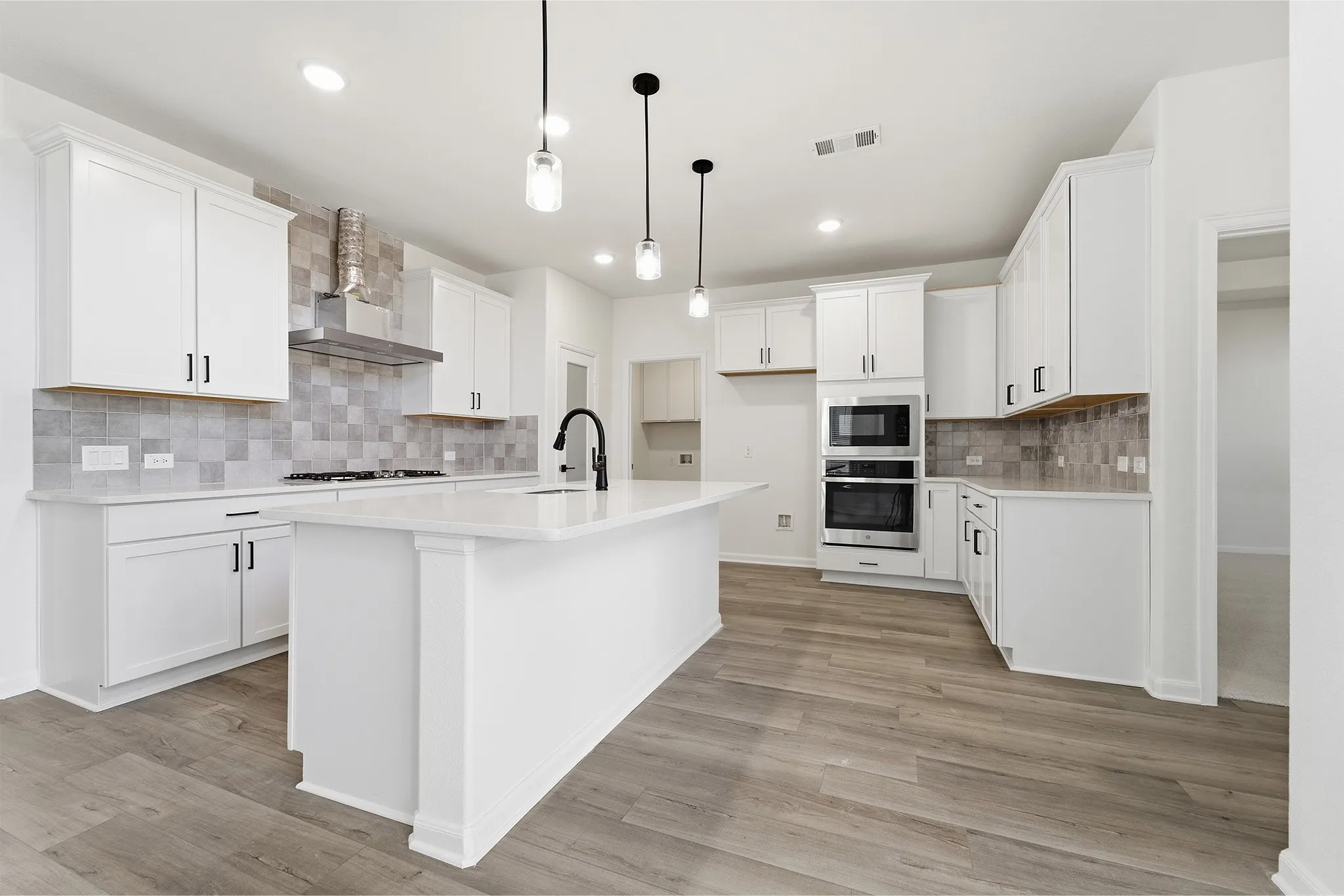 Bright kitchen featuring an island, white cabinetry, integrated stainless steel appliances, a tile backsplash, and wood-finish flooring