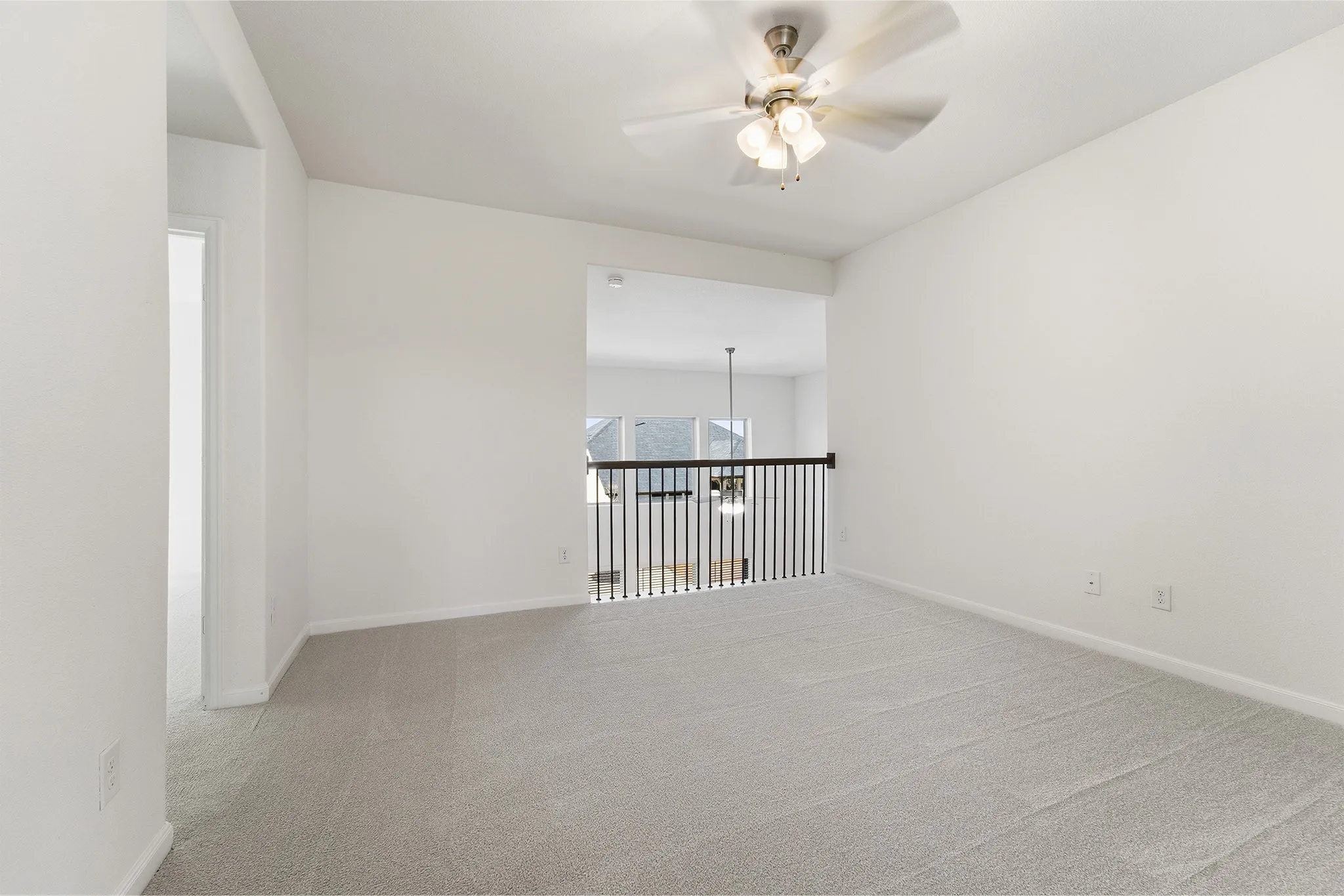 Carpeted loft area featuring a ceiling fan with integrated lighting and a wrought iron banister overlooking the lower level