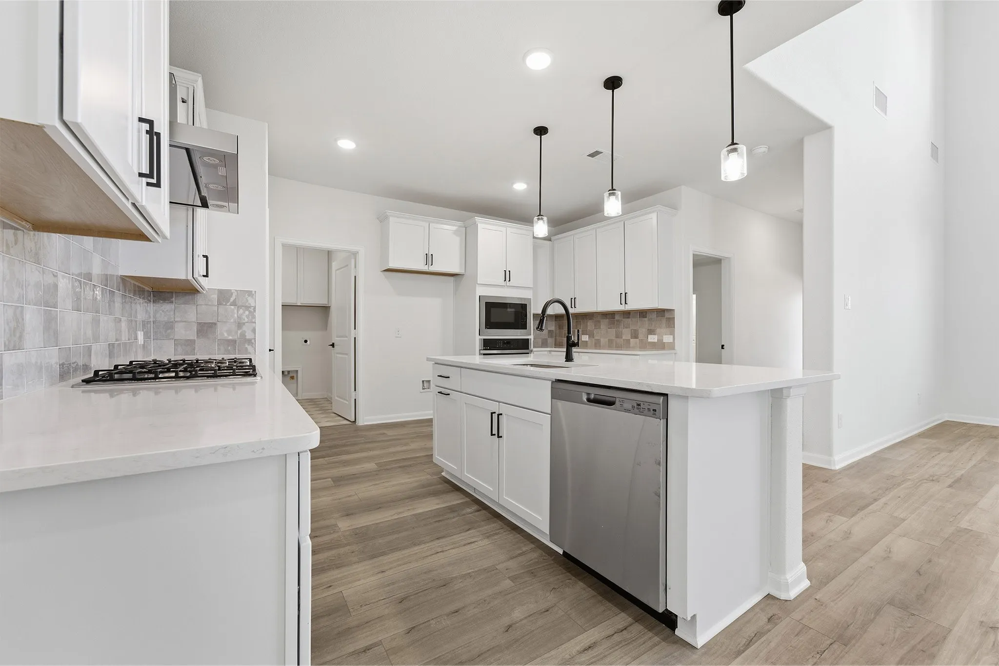Open-concept kitchen featuring white cabinetry, quartz countertops, a stone tile backsplash, a center island with pendant lighting, and wood-finish flooring