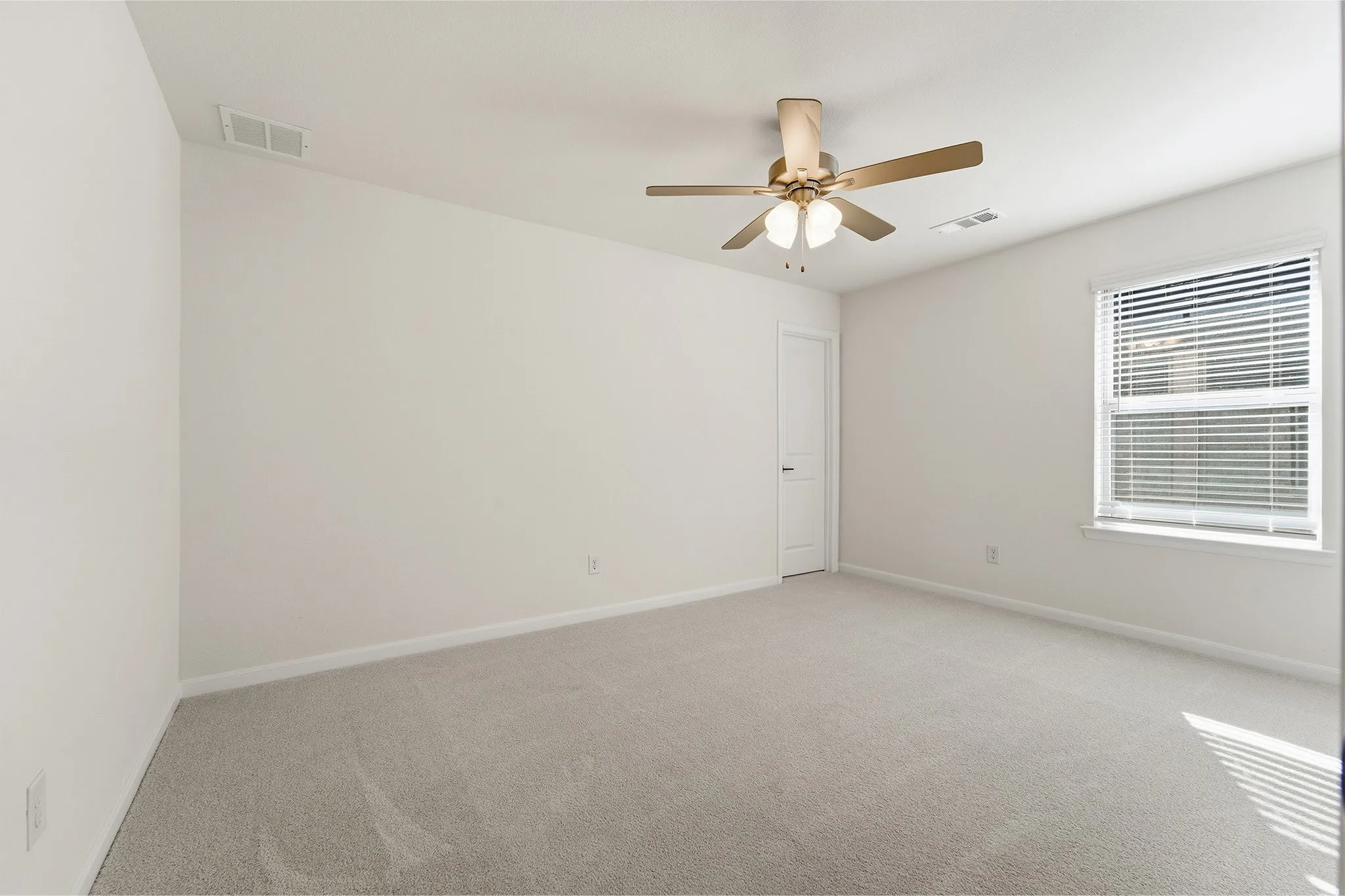 Expansive room featuring light-colored carpeting, a window with blinds, a white paneled door, and a ceiling fan with integrated lighting