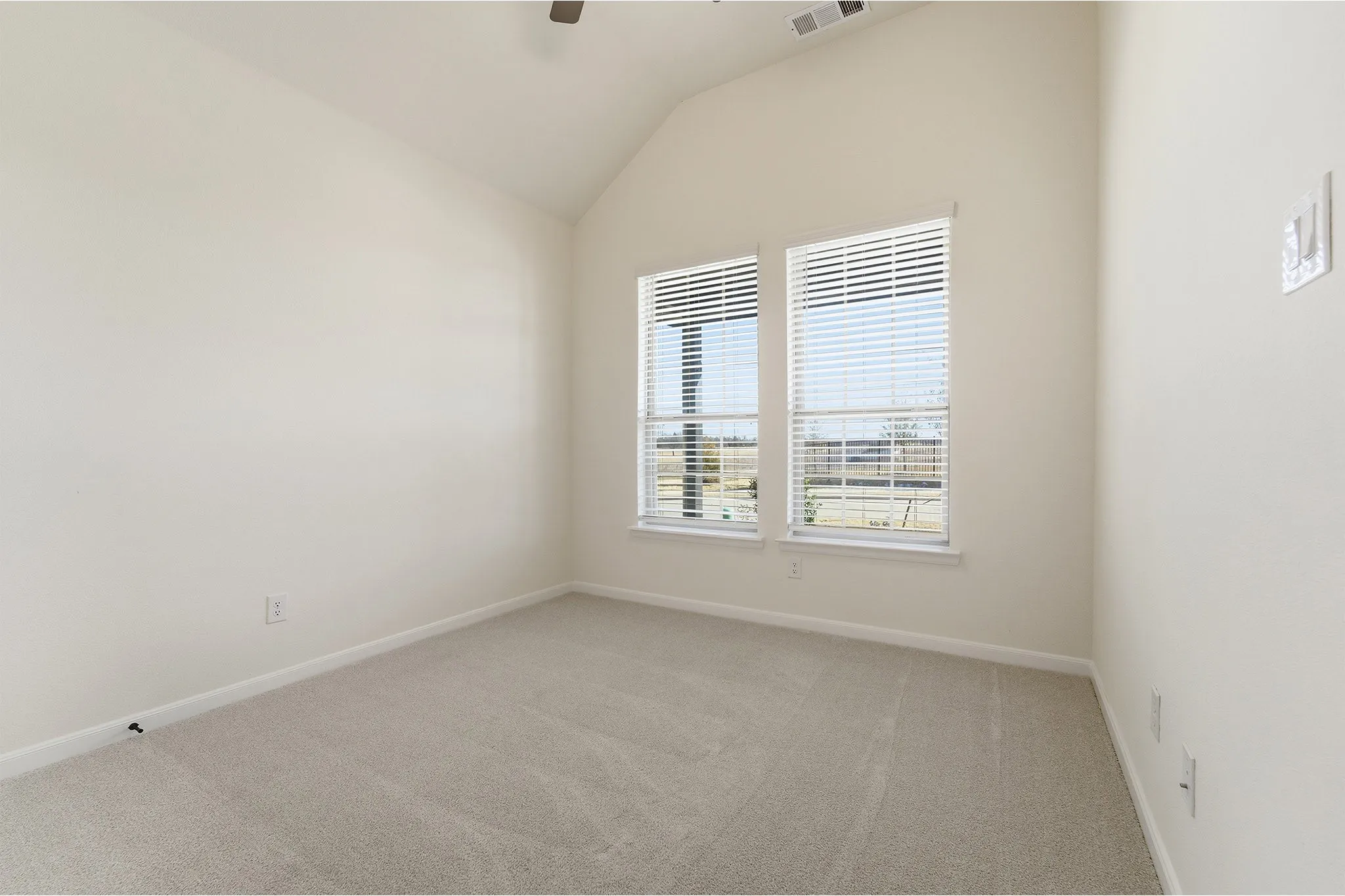 Vaulted ceiling, dual windows with blinds, light-colored carpet, and neutral wall tones