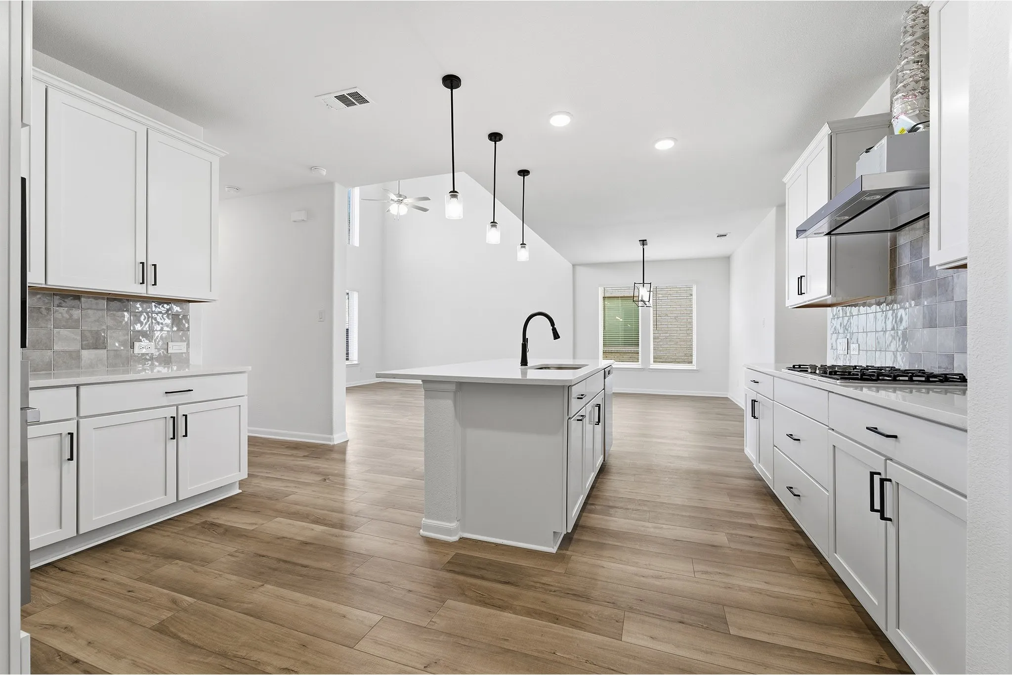 Modern kitchen featuring white cabinetry, a central island with a sink, stainless steel appliances, and wood-finish flooring