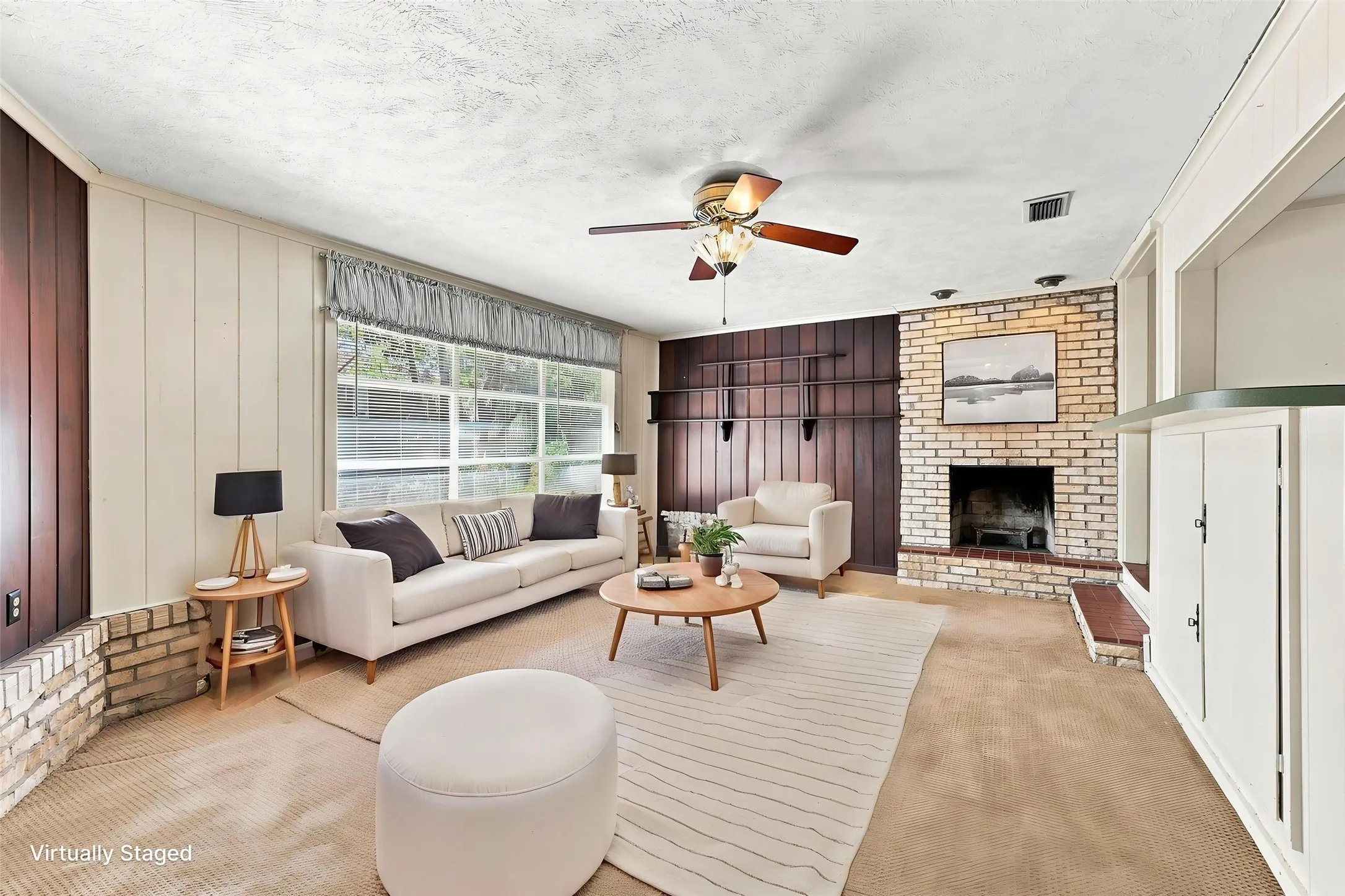 Living area featuring a brick fireplace, wood paneling, an exposed brick accent wall, and a wood-burning fireplace.