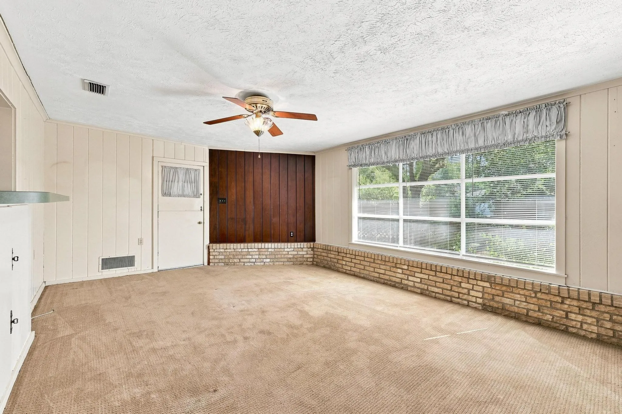 Flush ceiling fan, wood panel accent wall, brick accent wall, large picture window, and paneled walls.
