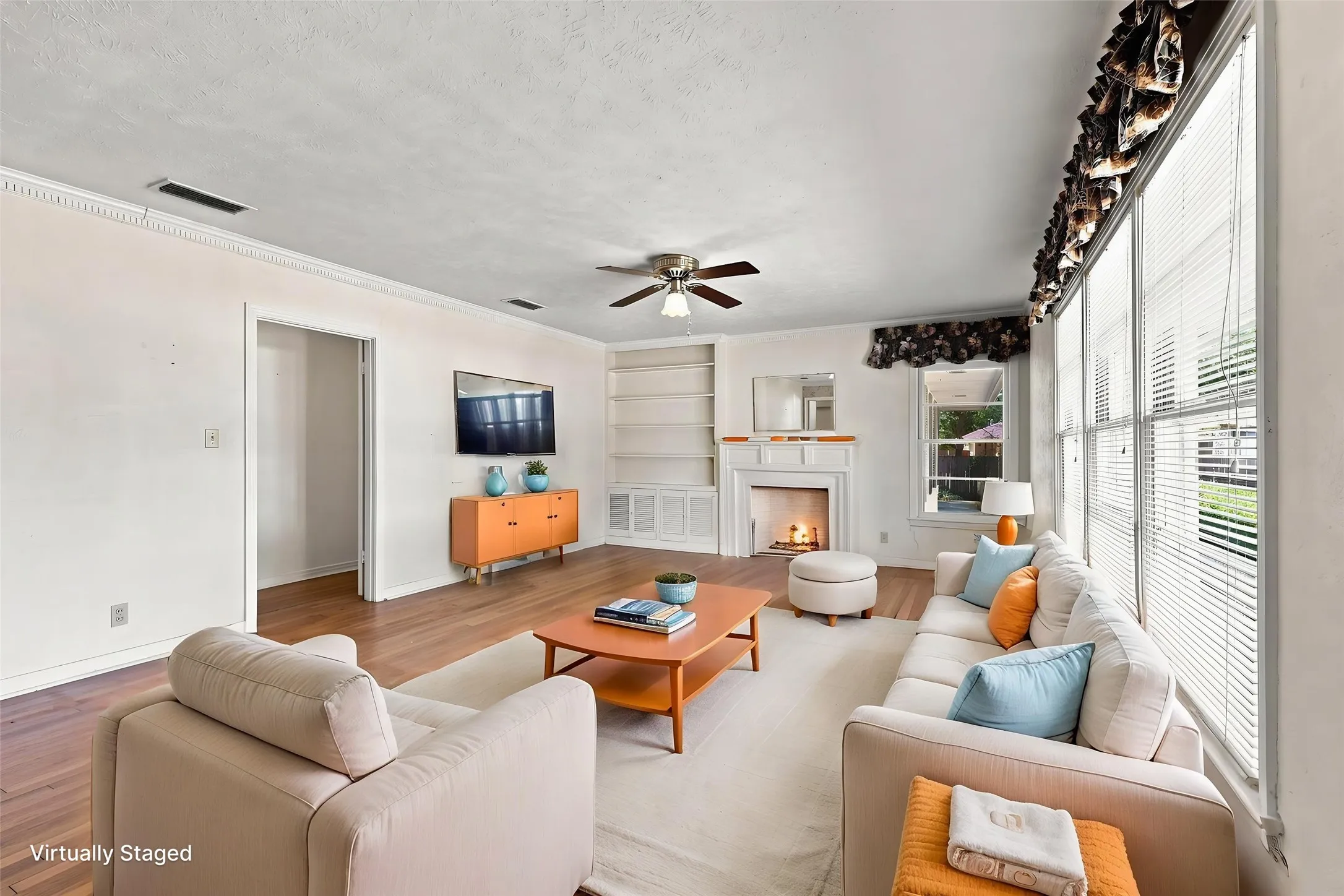 Hardwood flooring, white crown molding, built-in shelving, a faux fireplace with a mantel, and a ceiling fan.