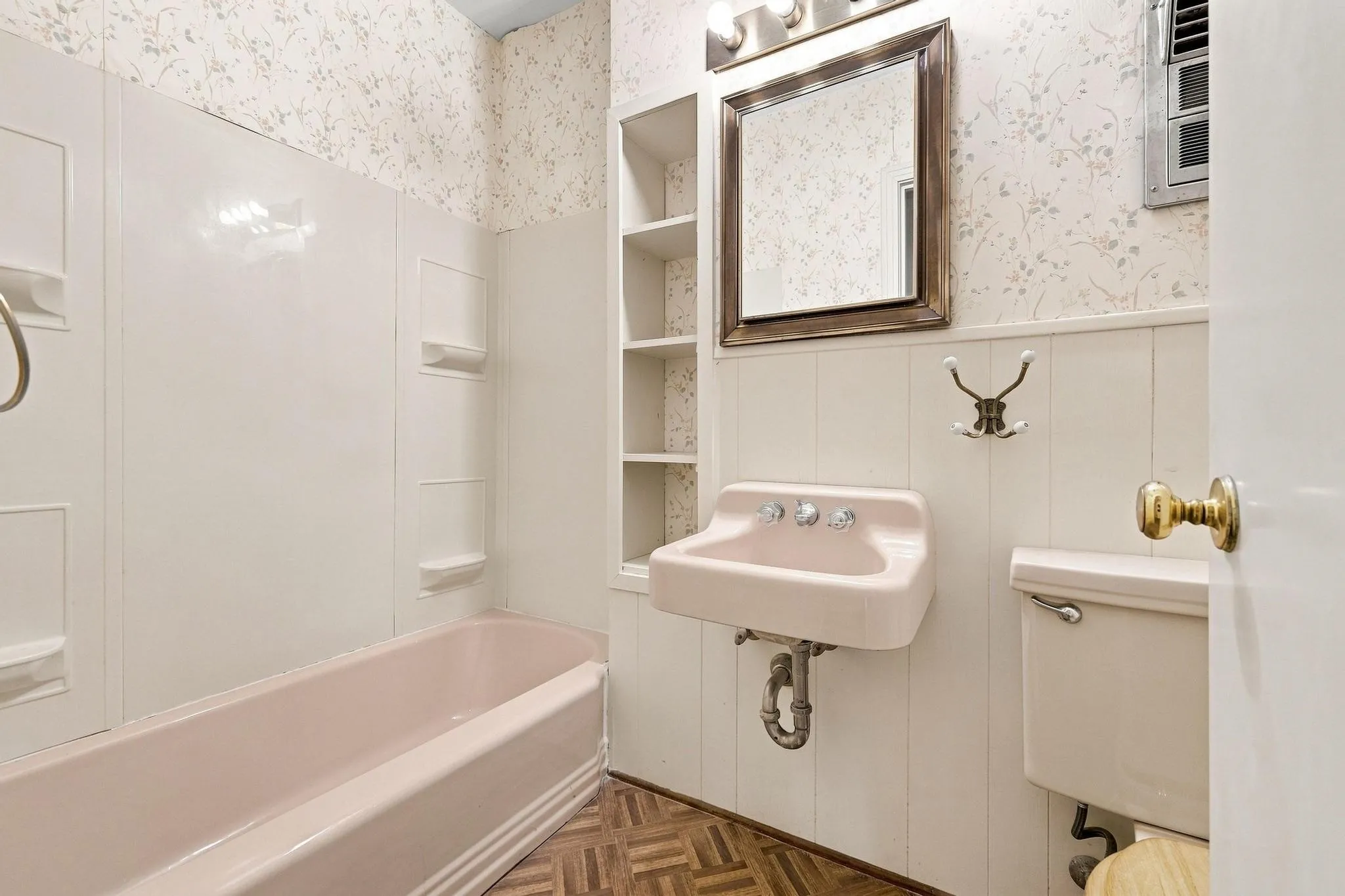 Pink porcelain bathtub and wall-mounted sink with chrome fixtures.