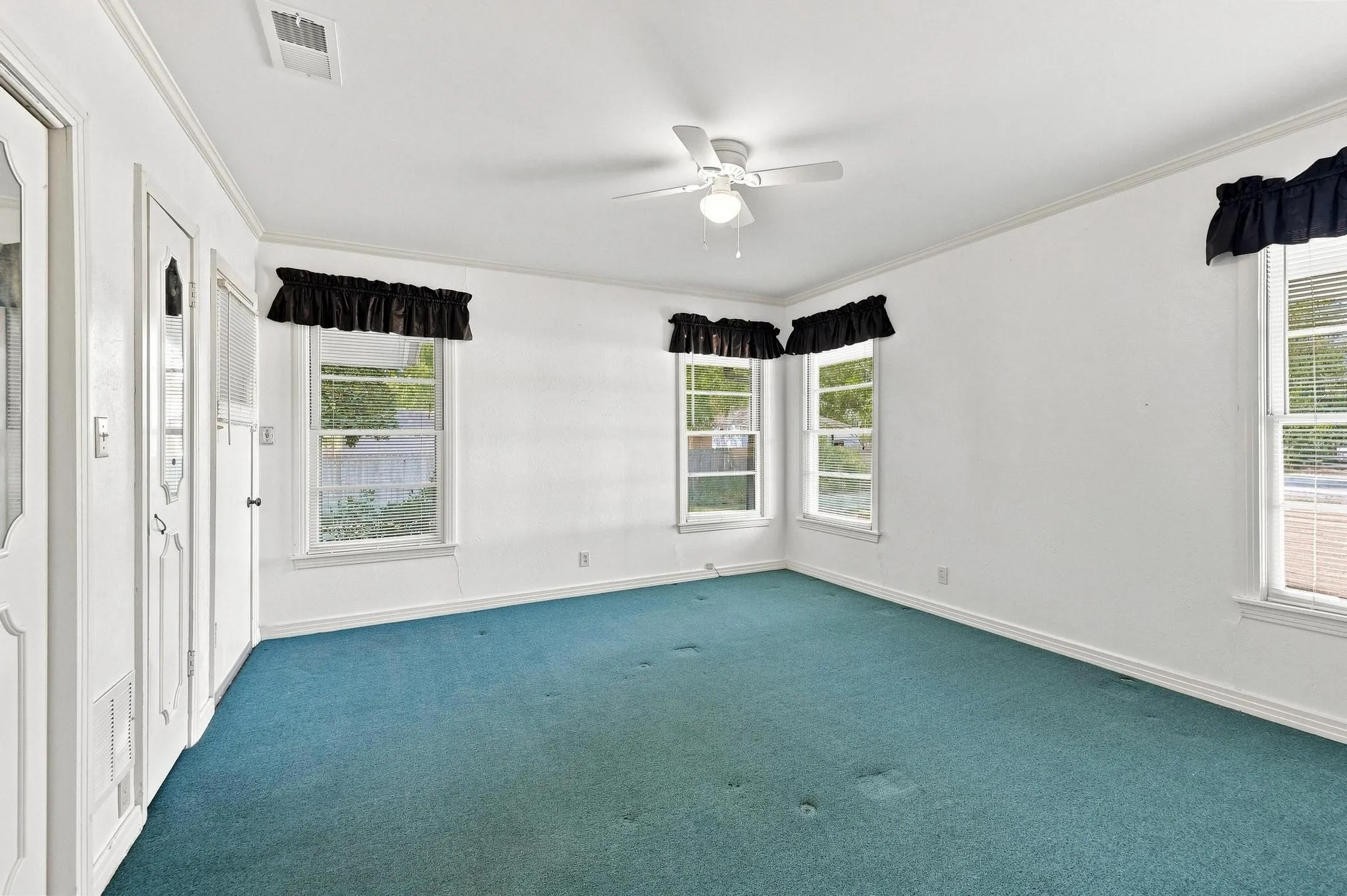 Multiple windows, ceiling fan, white interior walls, crown molding, and teal carpeting. Door leads to screened porch.