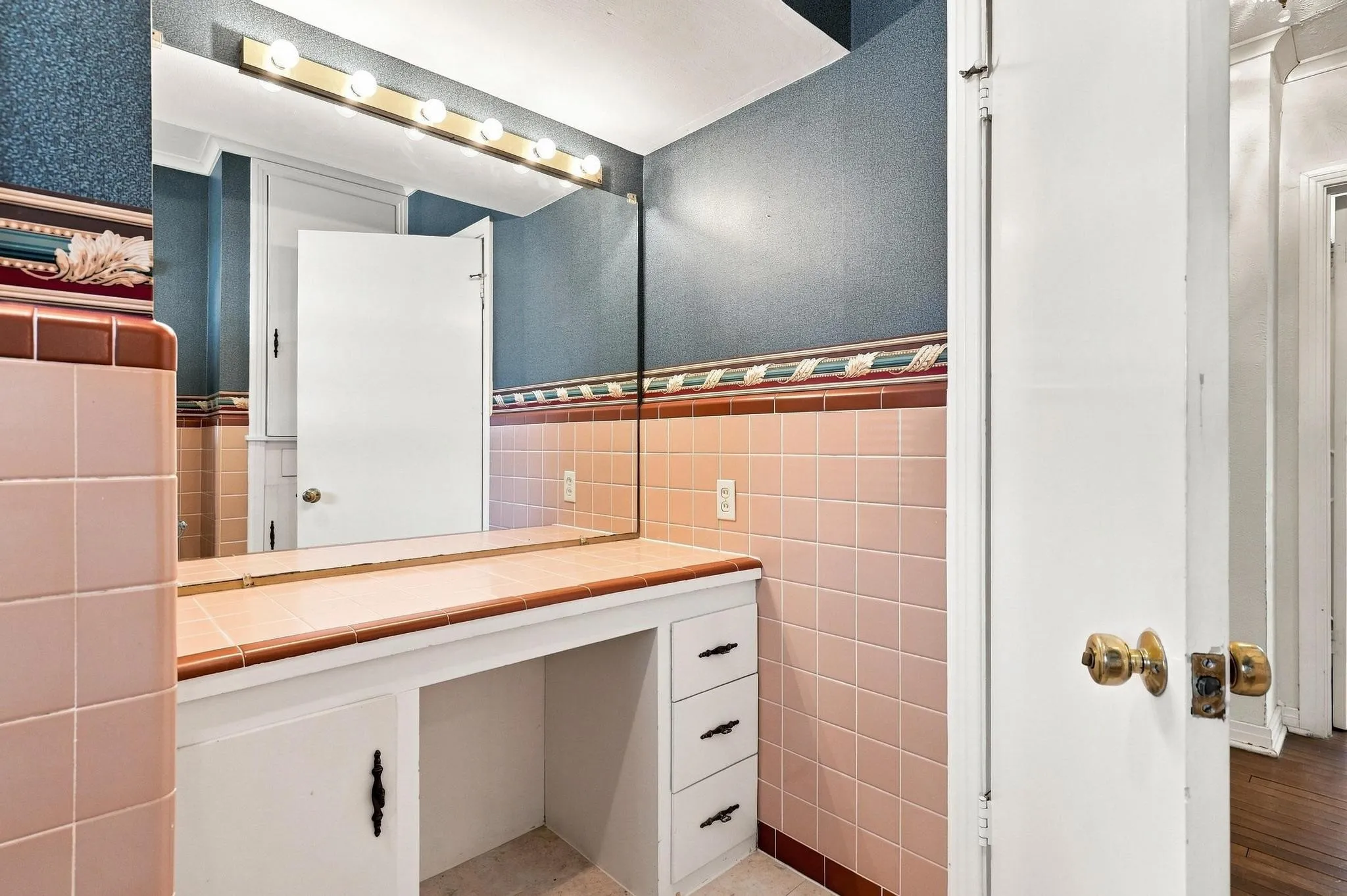Built-in vanity with tiled countertop, large wall-mounted mirror, and vanity lighting, which can be turn on/off by switching the lever on the right side of the light casing.