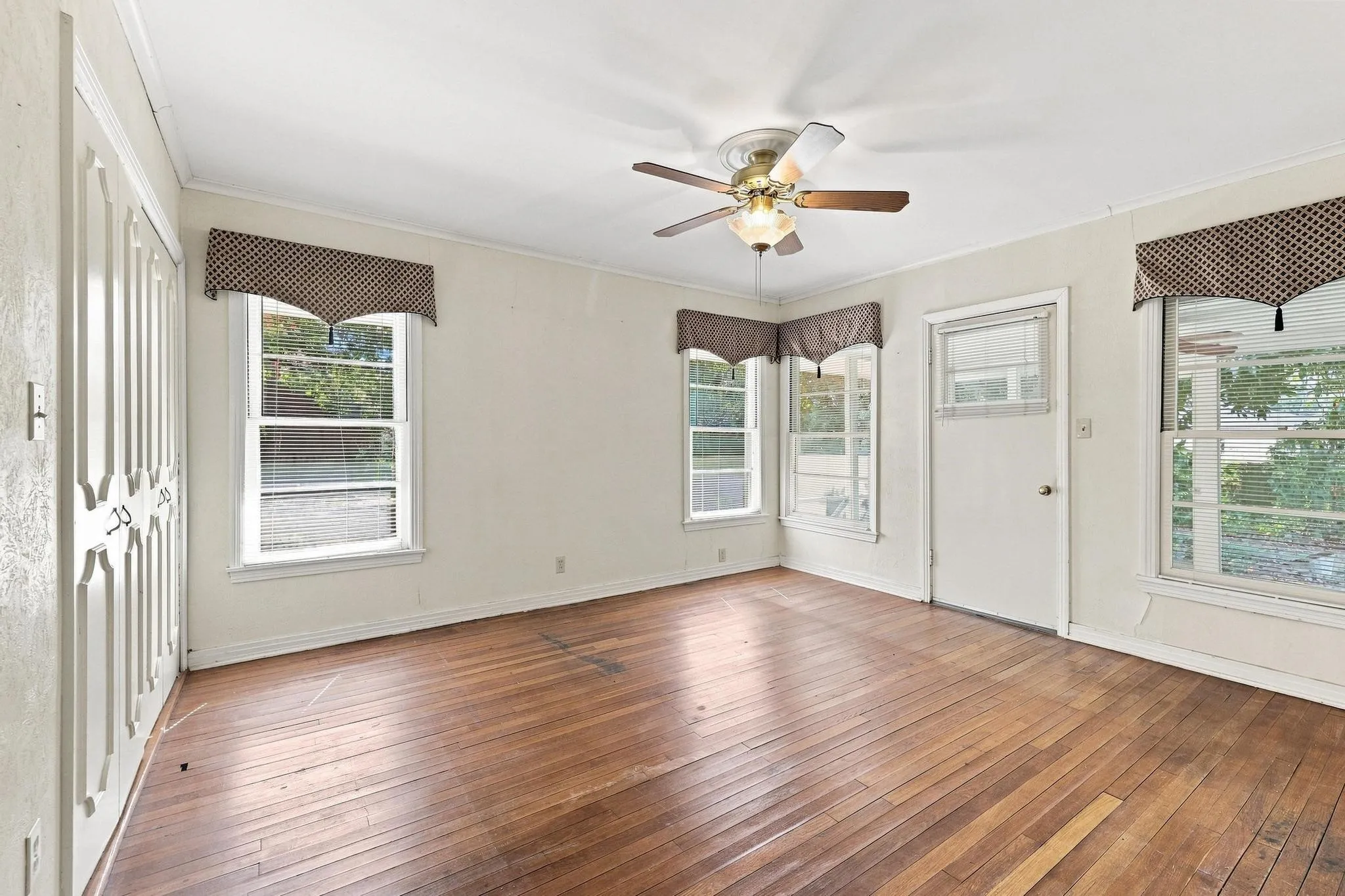 Hardwood flooring, multiple windows, ceiling fan, white paneled door, and closet with paneled bifold doors.