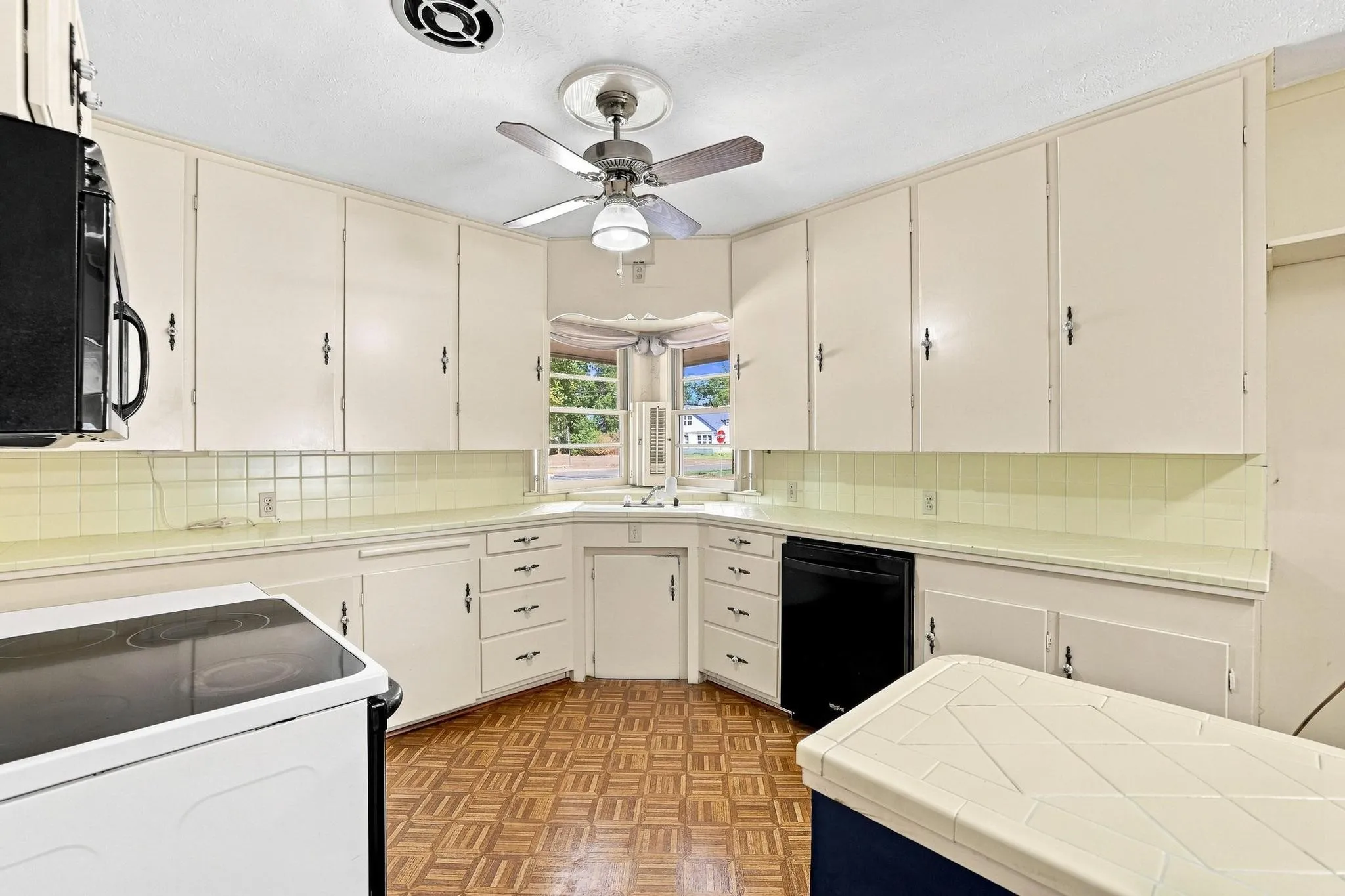 Kitchen featuring abundant white cabinetry, light-toned countertops, a light yellow tile backsplash, and vinyl flooring.