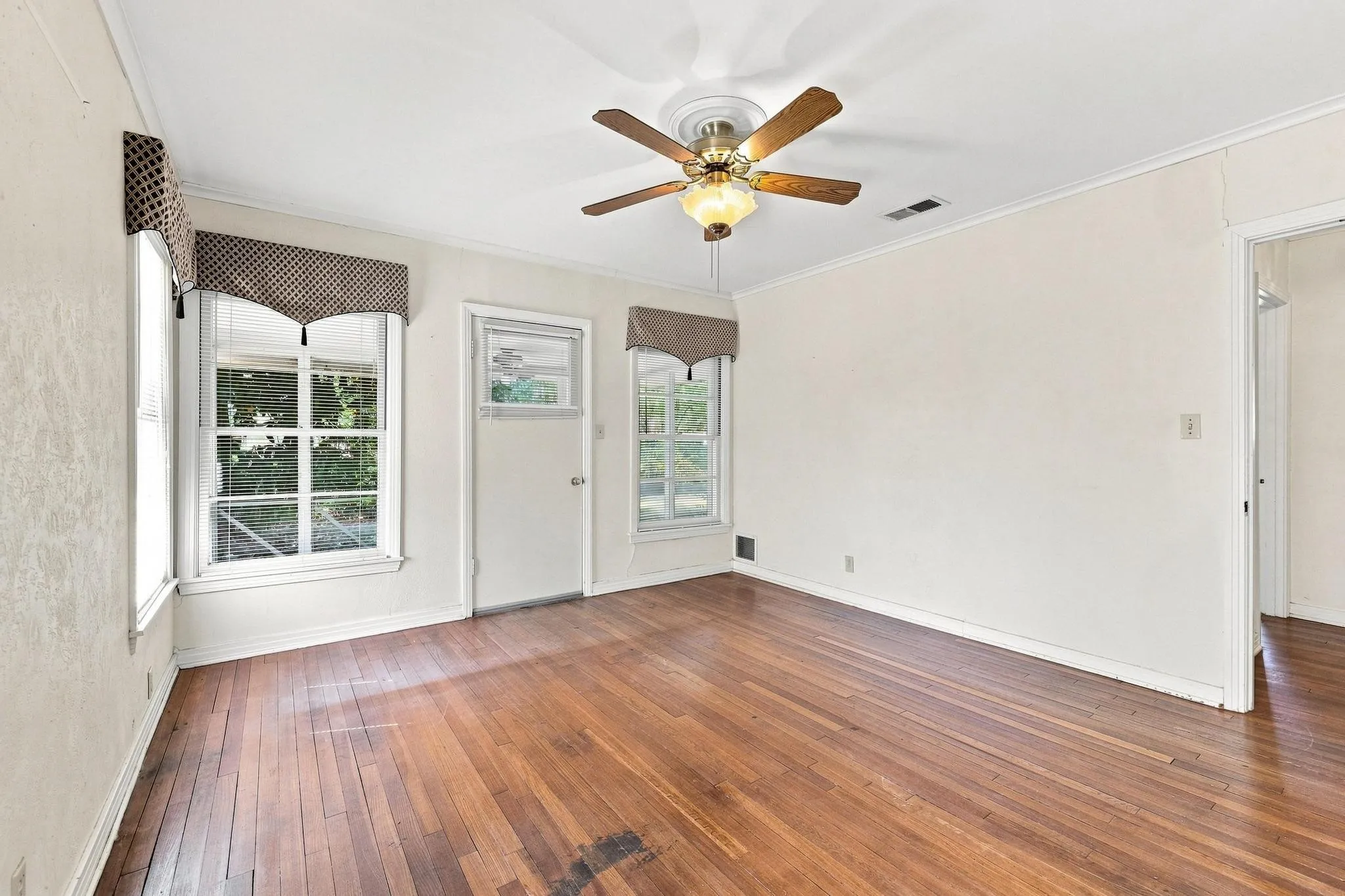 Hardwood flooring, multiple windows, ceiling fan with light fixture, and crown molding.