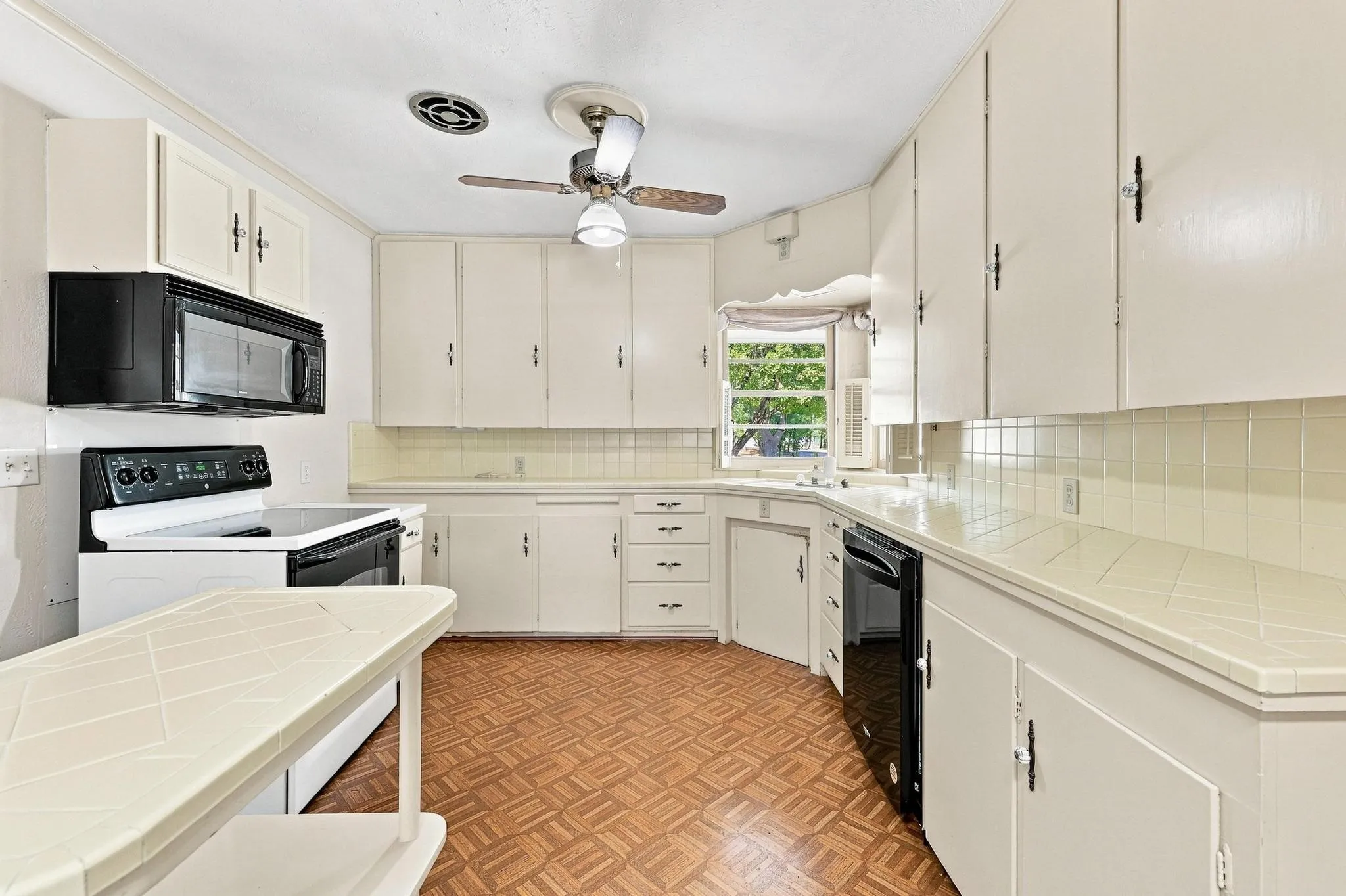 White cabinetry, tile countertops, tile backsplash, built-in microwave, dishwasher, and stove.