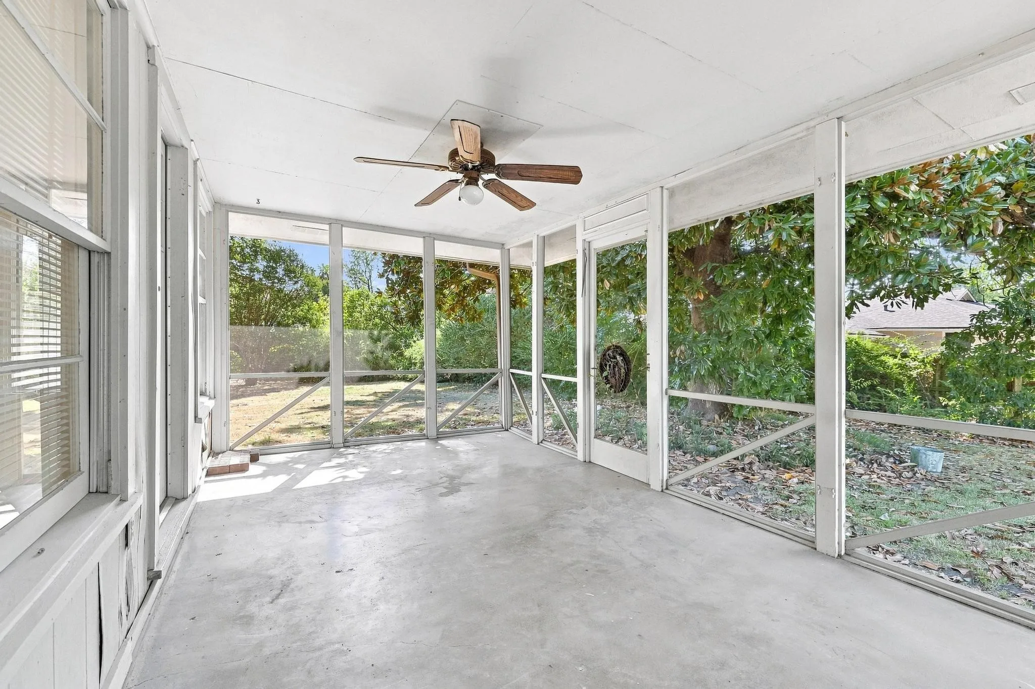 Screened porch with concrete flooring and a ceiling fan.