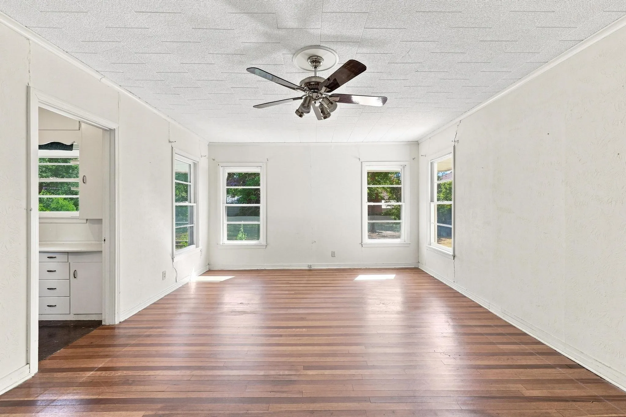 Hardwood flooring, multiple windows providing natural light, white painted walls, and ceiling fan with integrated lighting.