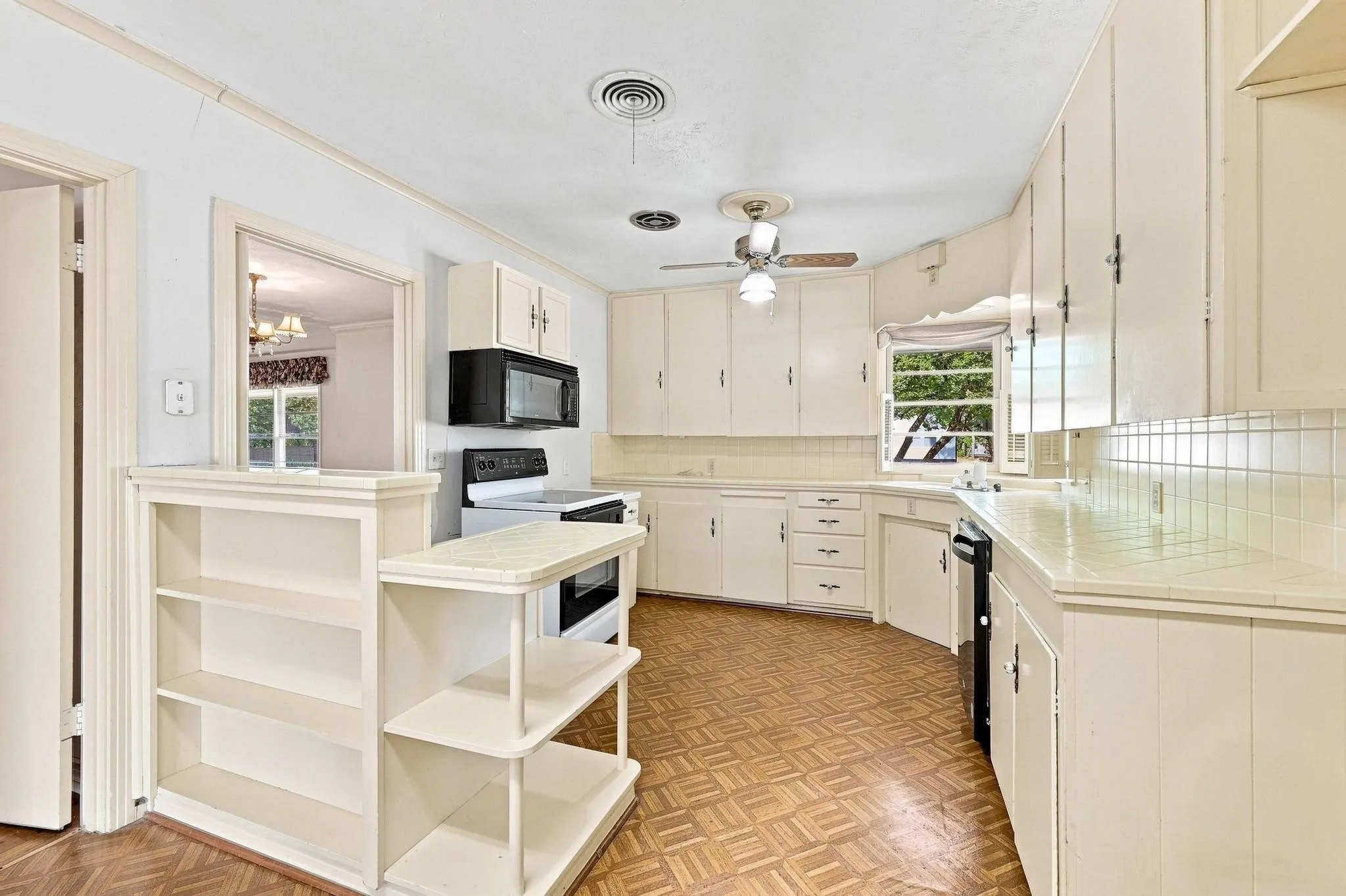 Kitchen featuring white cabinetry, tile backsplash, built-in shelving, a ceiling fan, and a window above the sink.