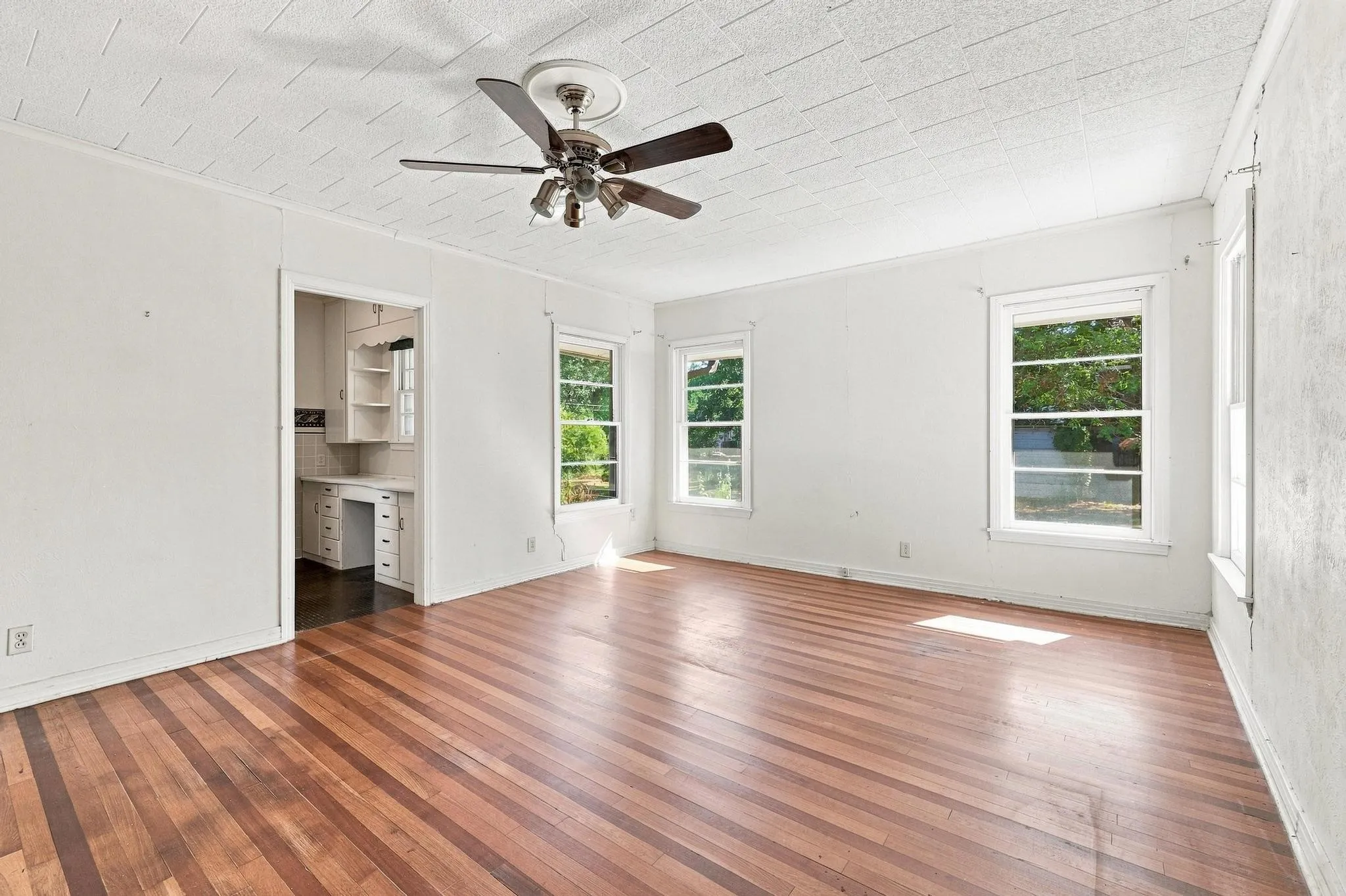 Hardwood flooring, painted white walls, ceiling fan with light fixture, and multiple windows.