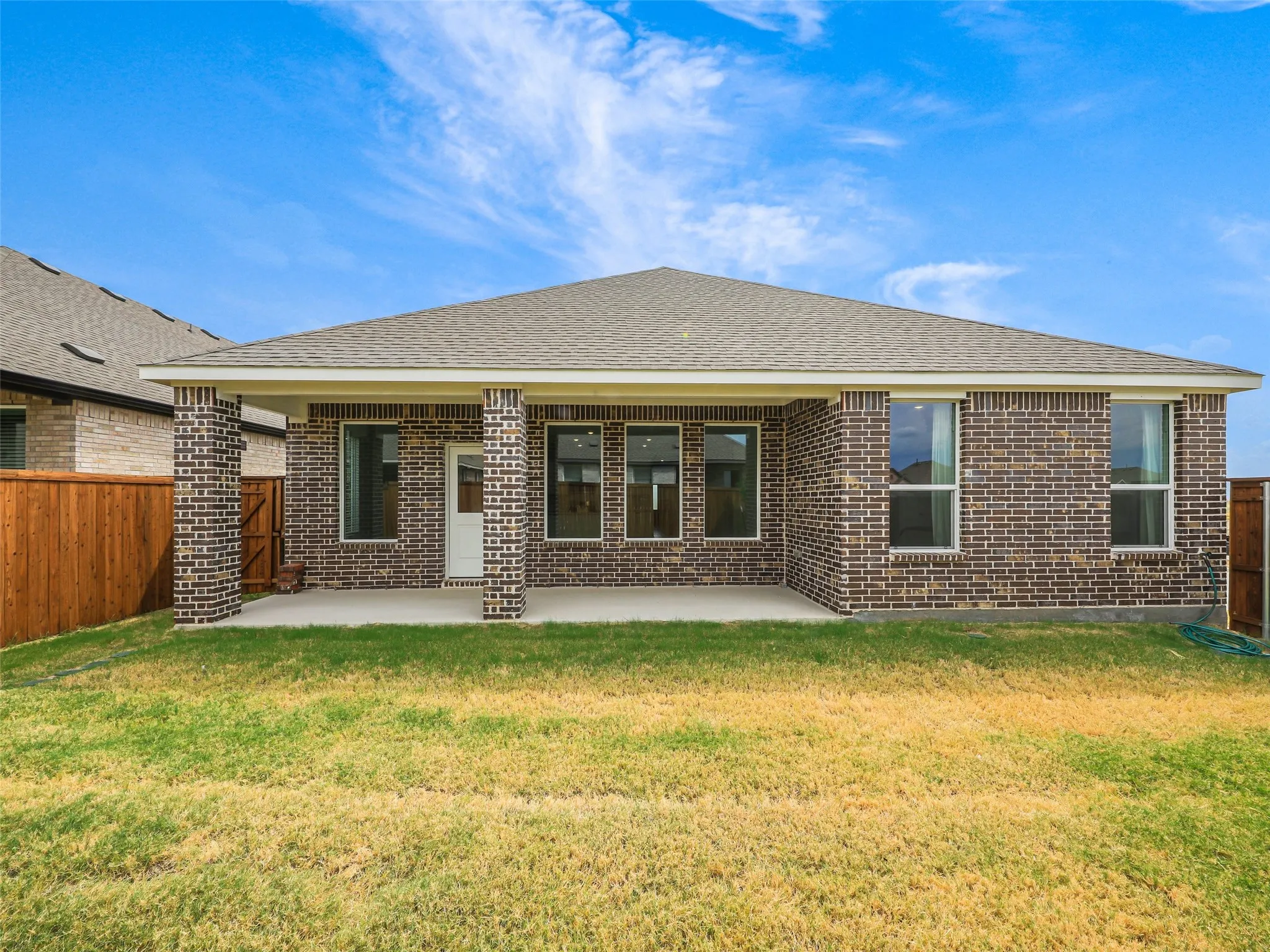 Rear exterior featuring a covered patio, dark brick facade, multiple windows, and a wood privacy fence