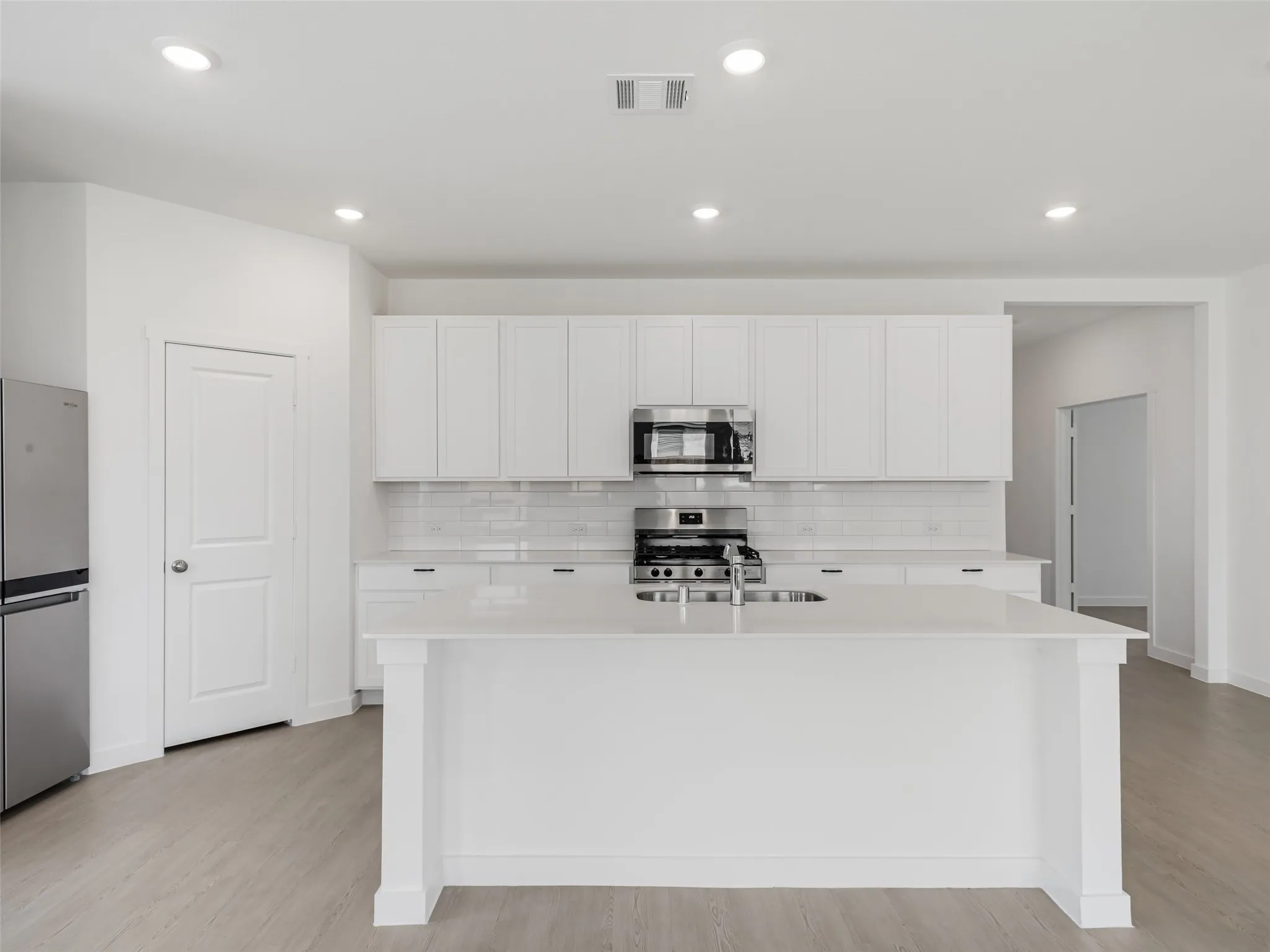 Contemporary kitchen featuring white cabinetry, a large center island, stainless steel appliances, recessed lighting, and wood-finish flooring
