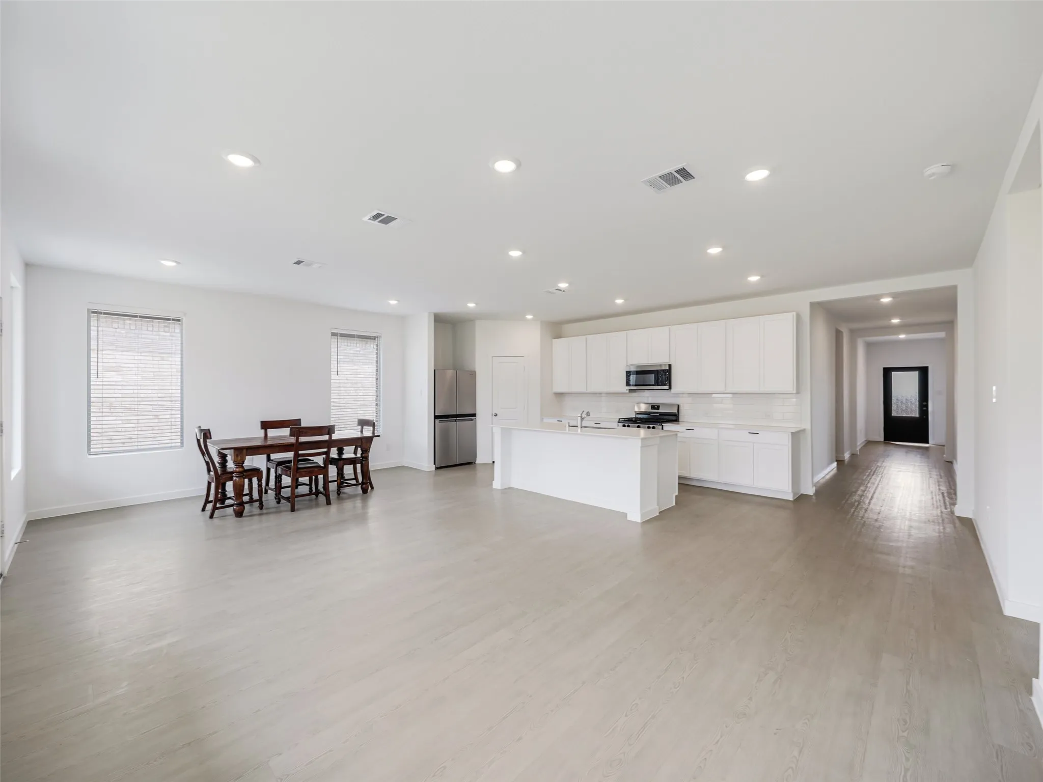 Open-concept living and kitchen area featuring recessed ceiling lighting, white cabinetry with stainless steel appliances, wood-finish flooring throughout, and abundant natural light from multiple windows
