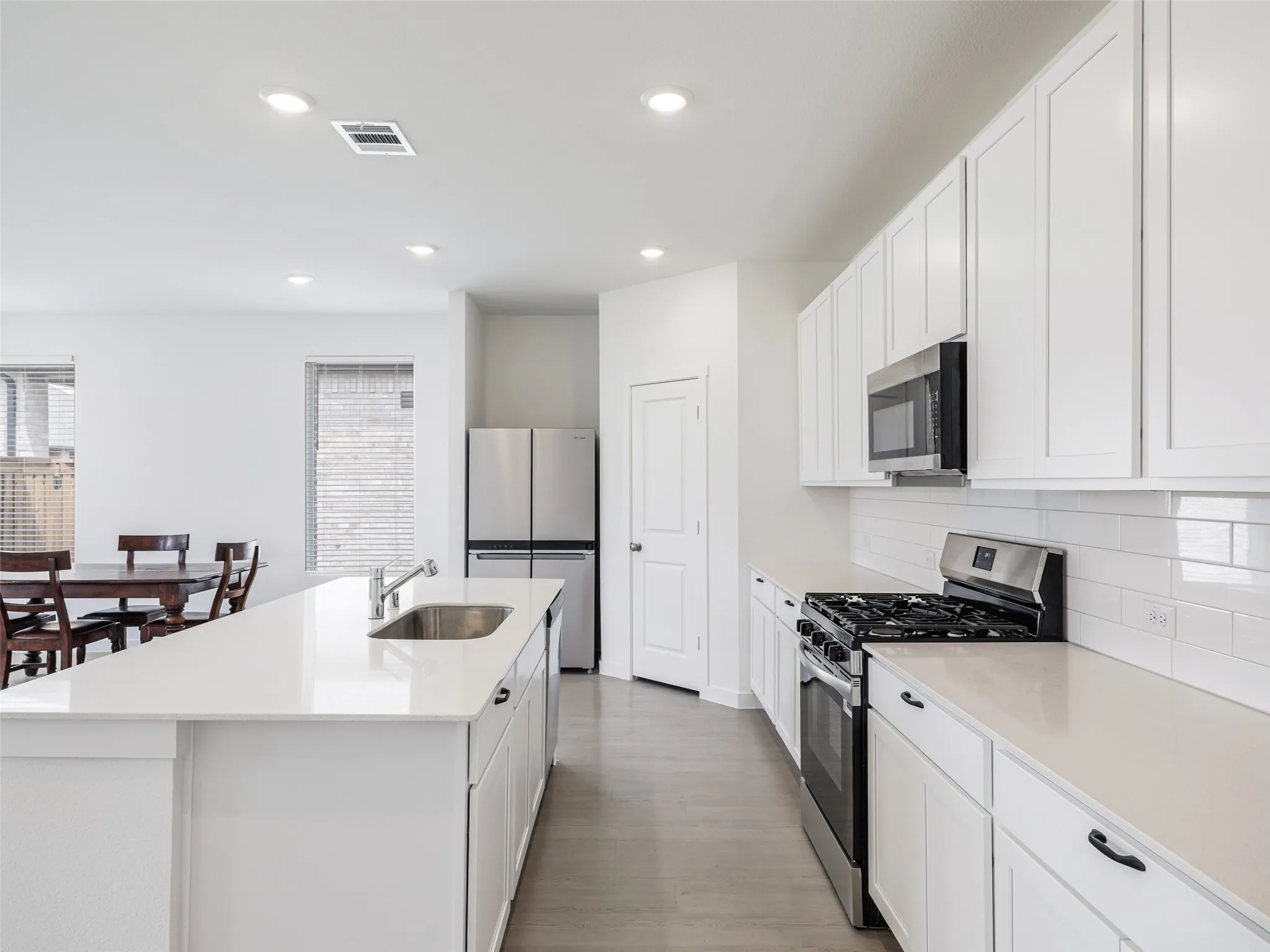 Modern kitchen featuring white shaker cabinetry, stainless steel appliances, a center island with an undermount sink, and light-colored countertops