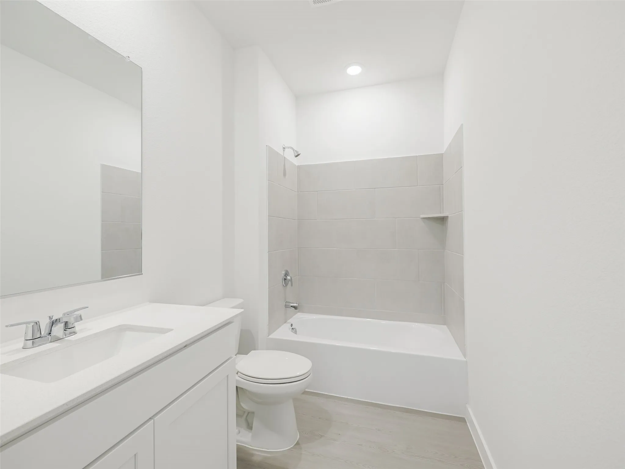 White vanity with integrated sink, rectangular mirror, chrome faucet, white bathtub with light-colored tile surround, recessed lighting