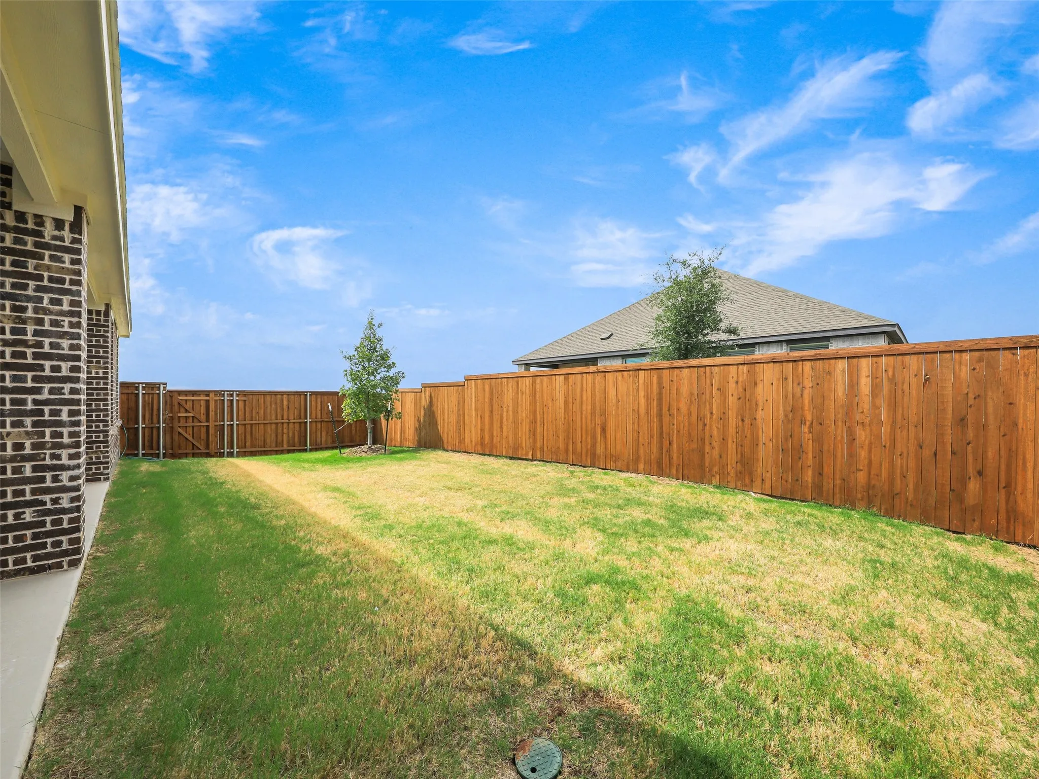 Expansive backyard featuring a manicured lawn, wood fencing, and a brick-clad exterior wall