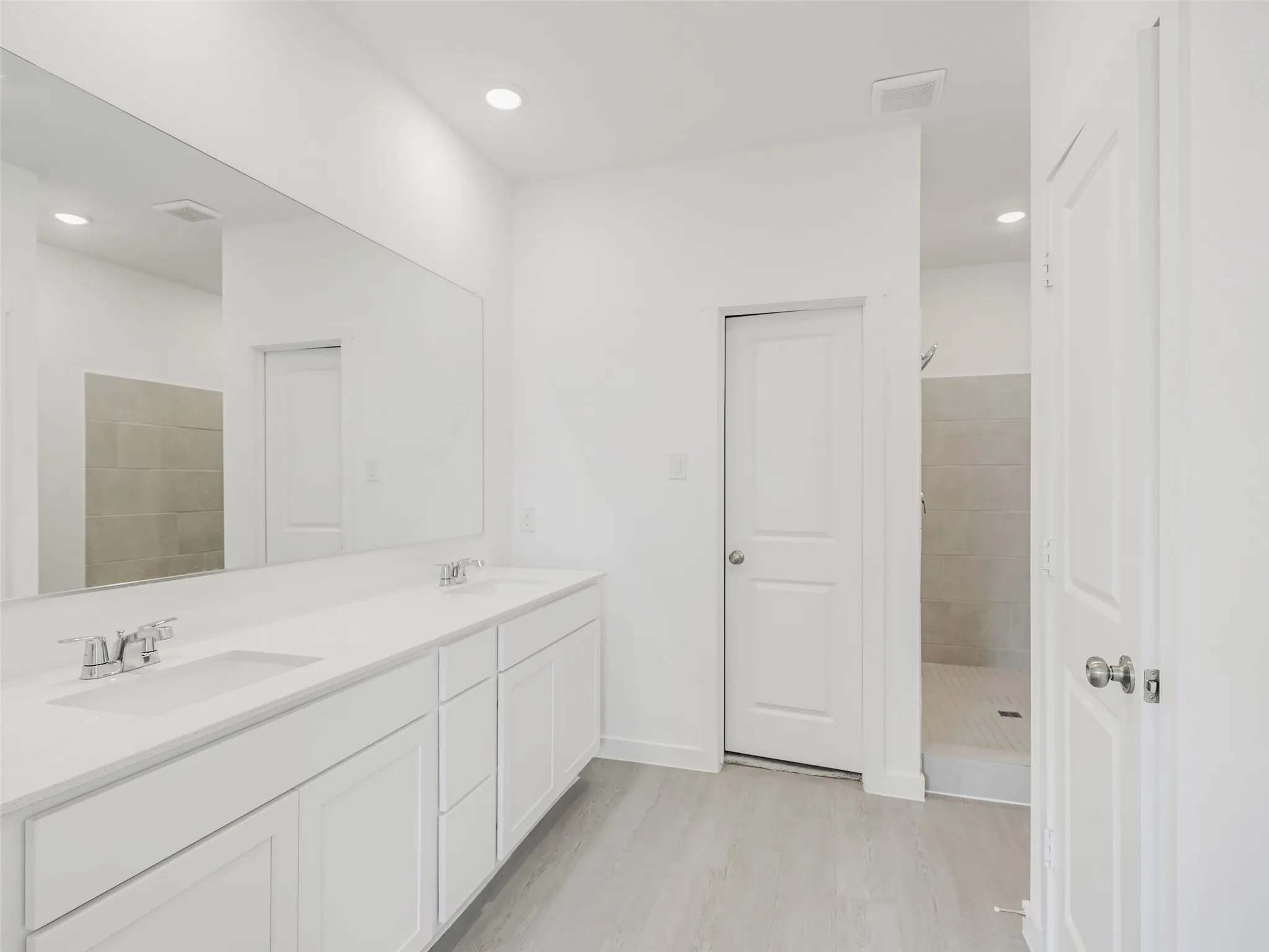 Dual vanity with white cabinetry, integrated sinks, chrome fixtures, and a spacious wall-mounted mirror