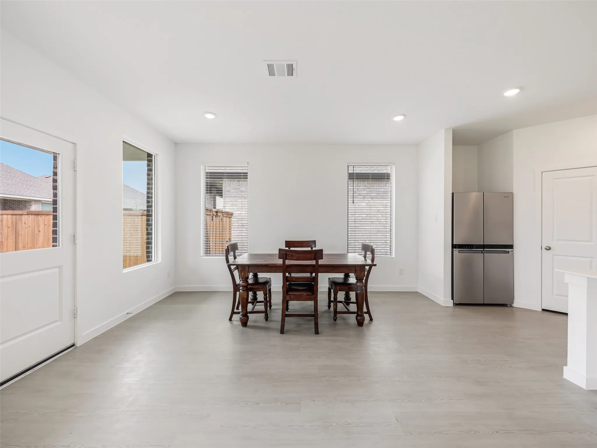 Open-concept living area with light-toned wood-finish flooring, recessed lighting, and multiple windows