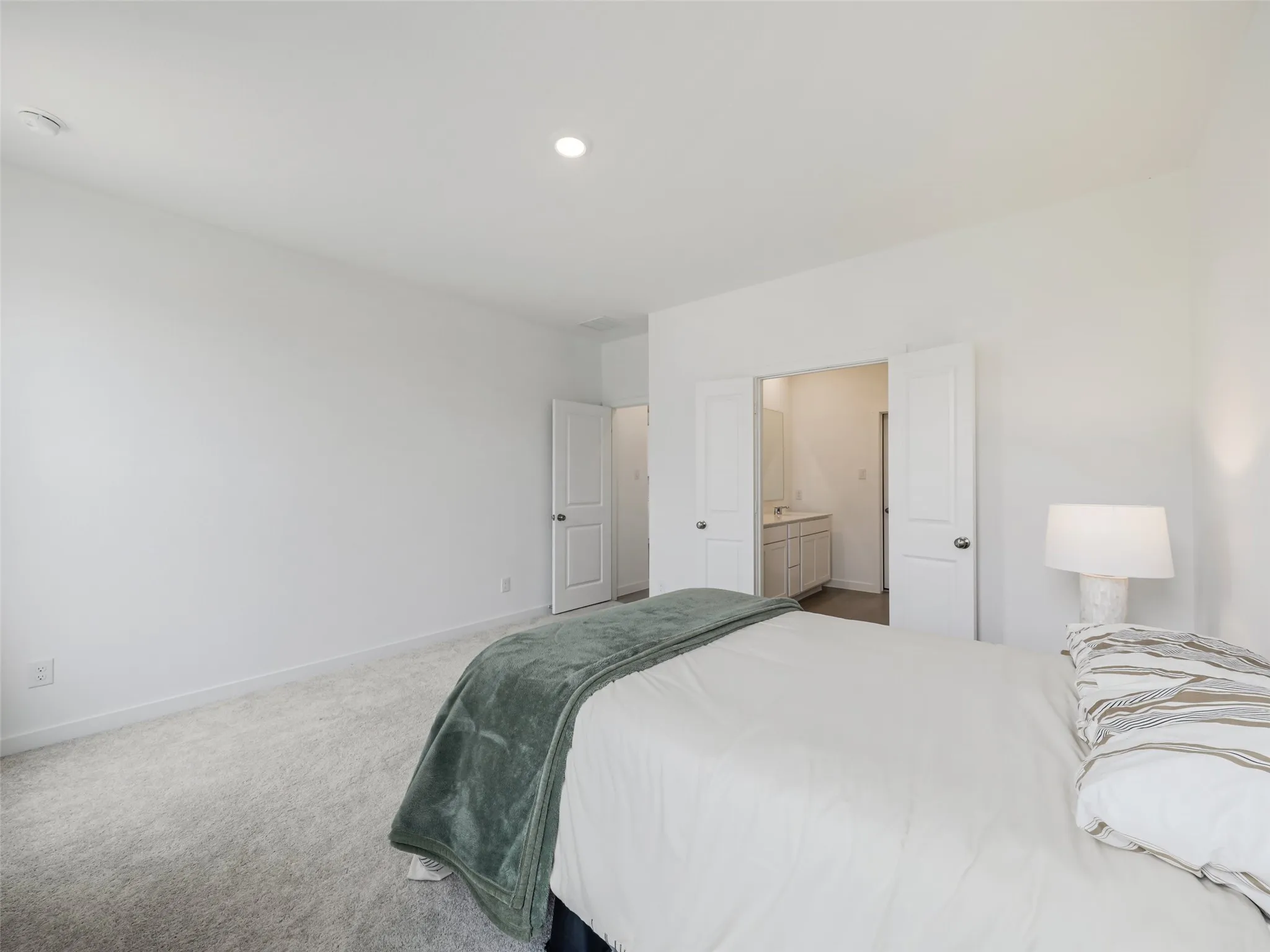 Recessed ceiling lighting, light gray wall-to-wall carpeting, white interior doors, and a double-door entryway to a bathroom with a vanity