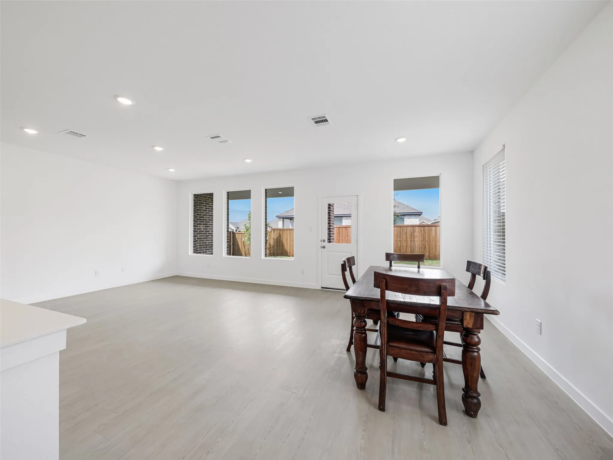 Recessed lighting, light wood-finish flooring, white walls, multiple windows, and a white door with a window