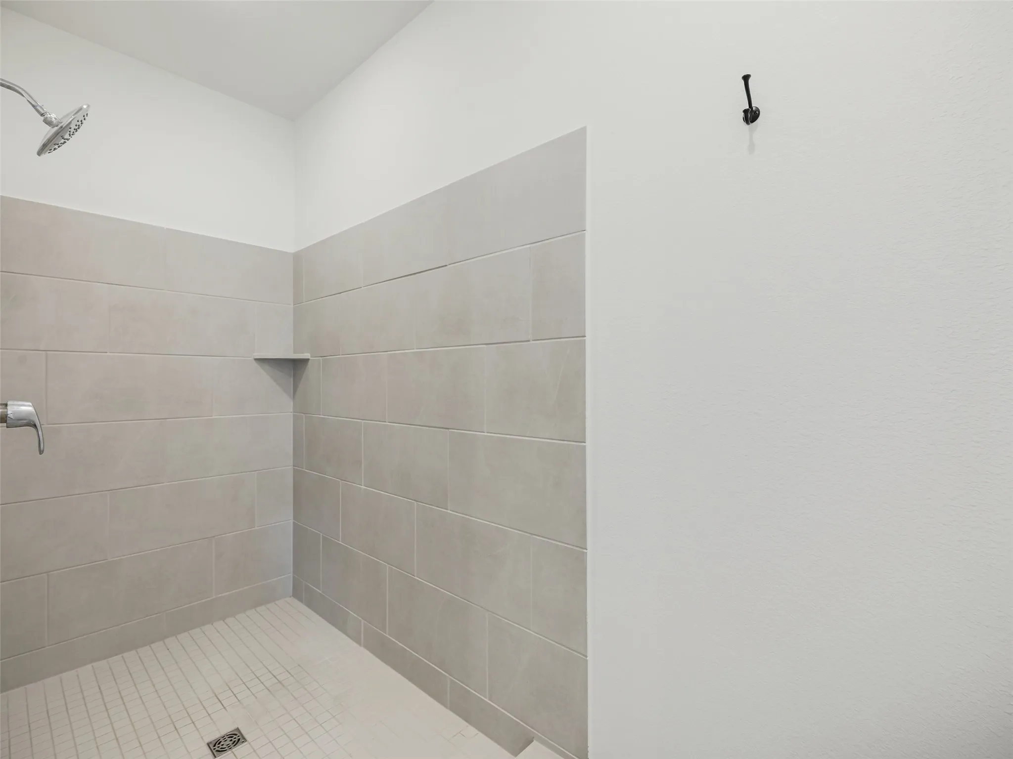 Shower enclosure featuring light-colored tile walls, a built-in corner shelf, and a textured white wall