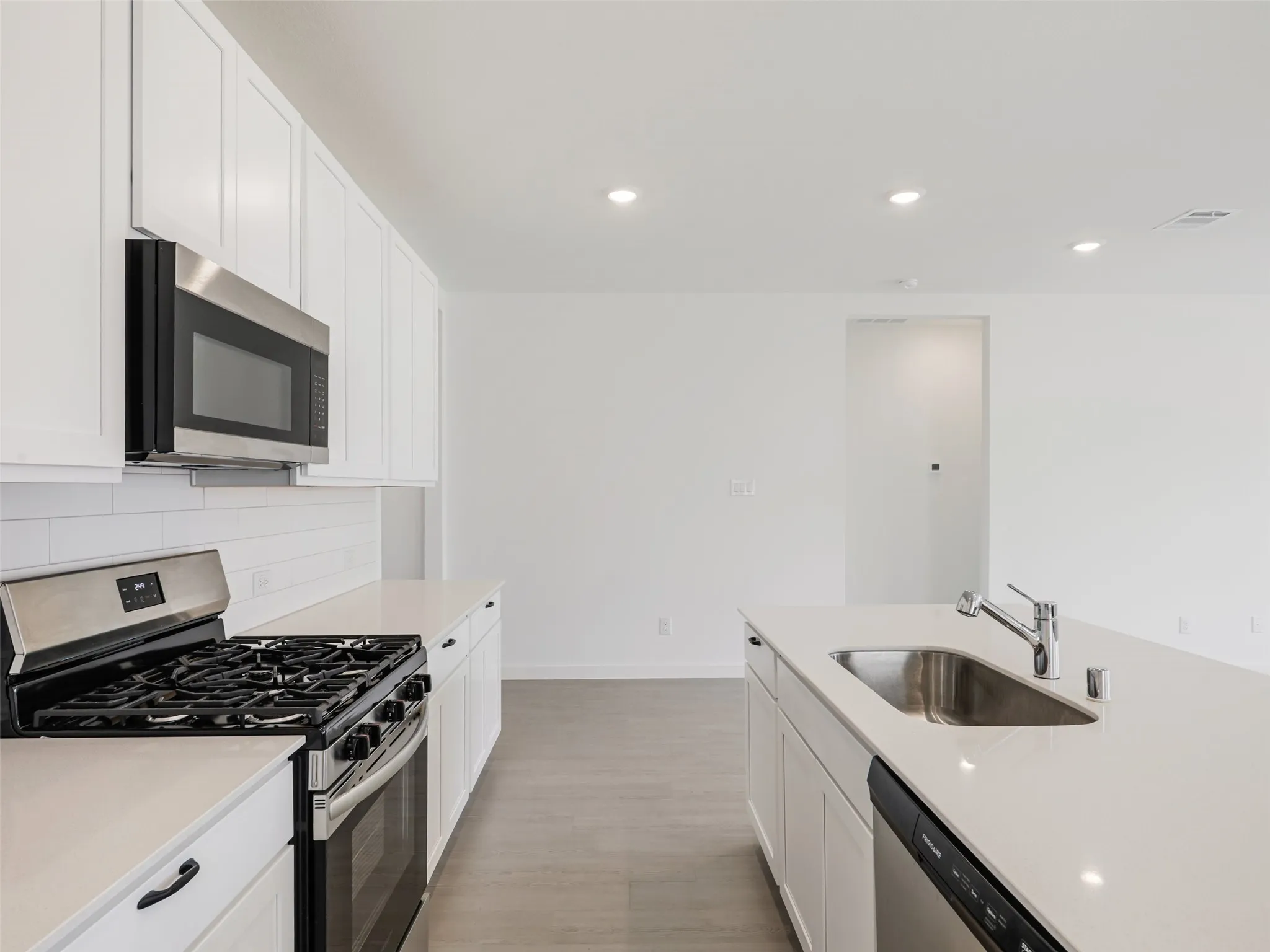 White cabinetry with black hardware, stainless steel appliances, solid surface countertops, light wood-finish flooring, and recessed ceiling lighting