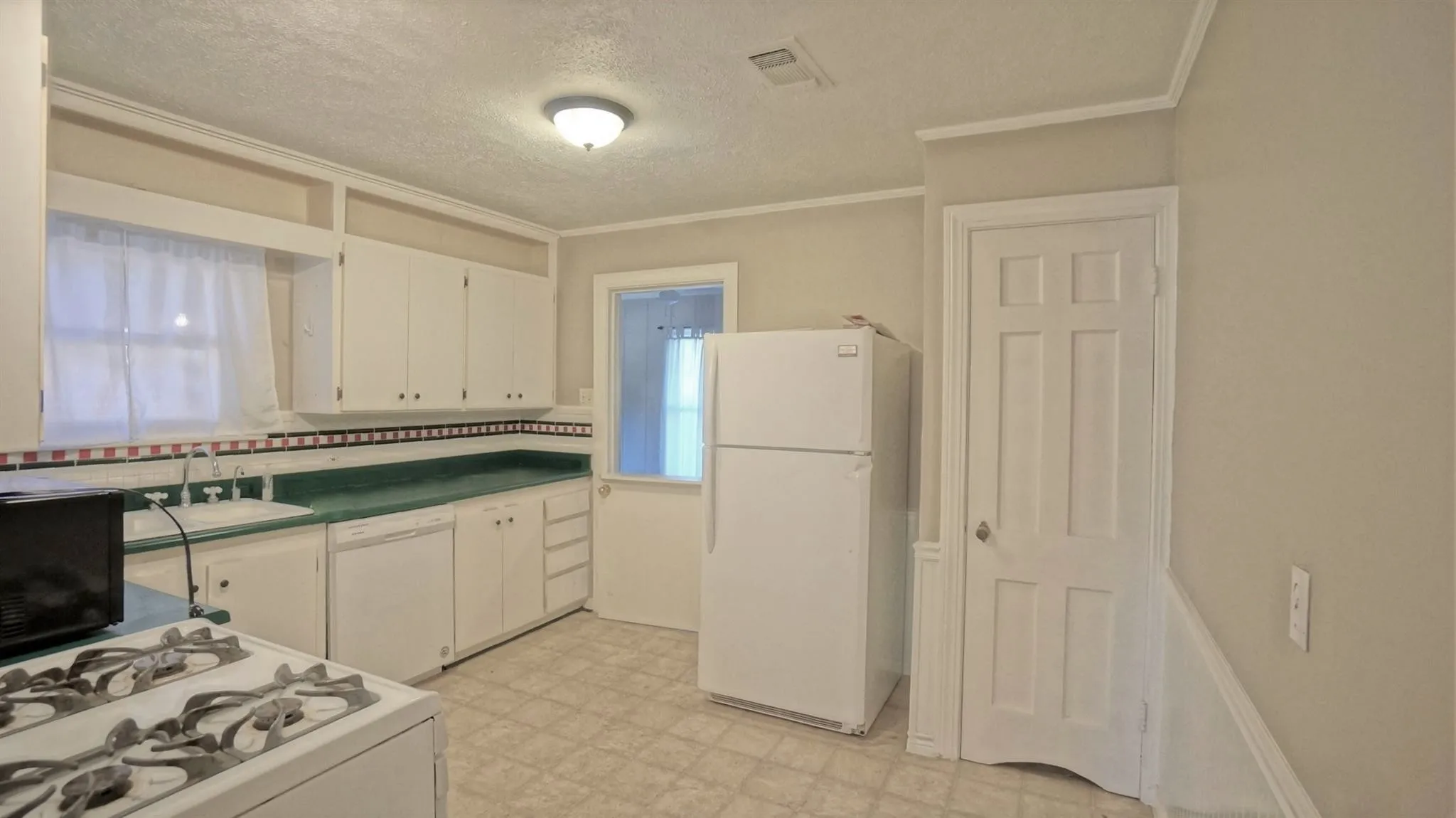 Kitchen with white appliances, light flooring, white cabinets, ornamental molding, and a textured ceiling