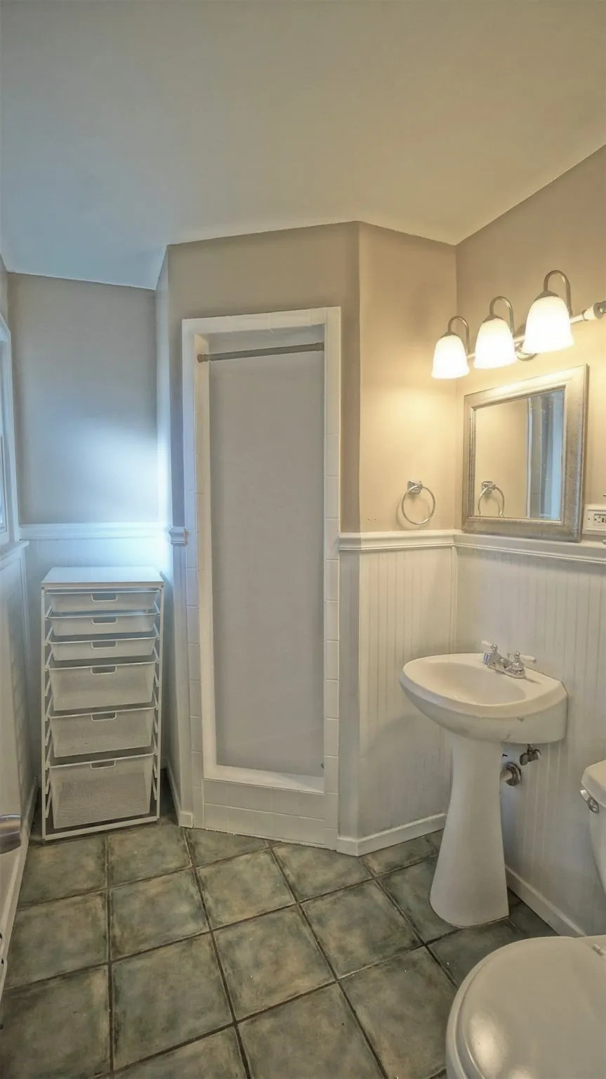Bathroom featuring a wainscoted wall, tile patterned flooring, and a shower stall