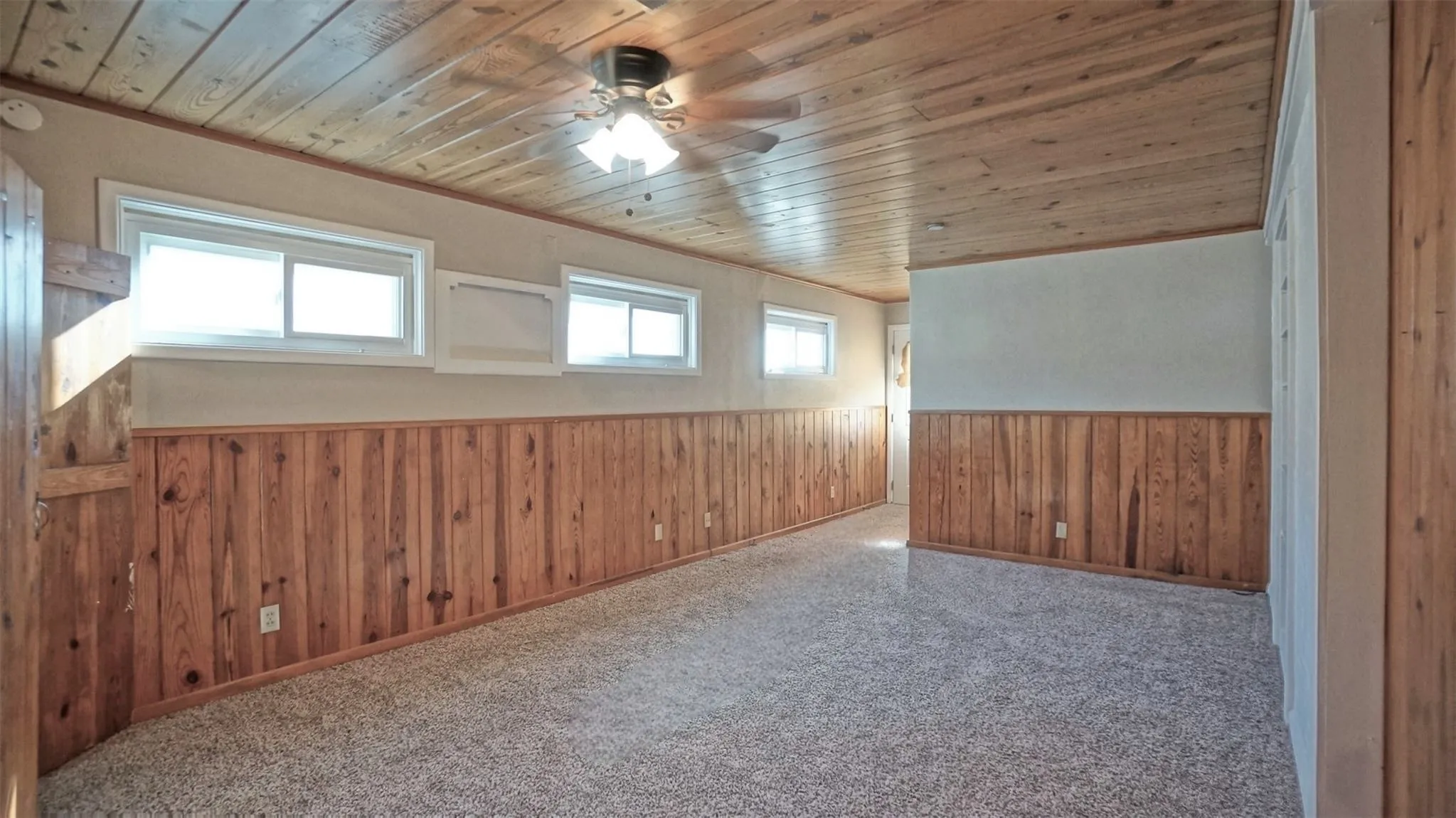 Unfurnished room featuring wooden ceiling, a wainscoted wall, wood walls, ceiling fan, and carpet flooring