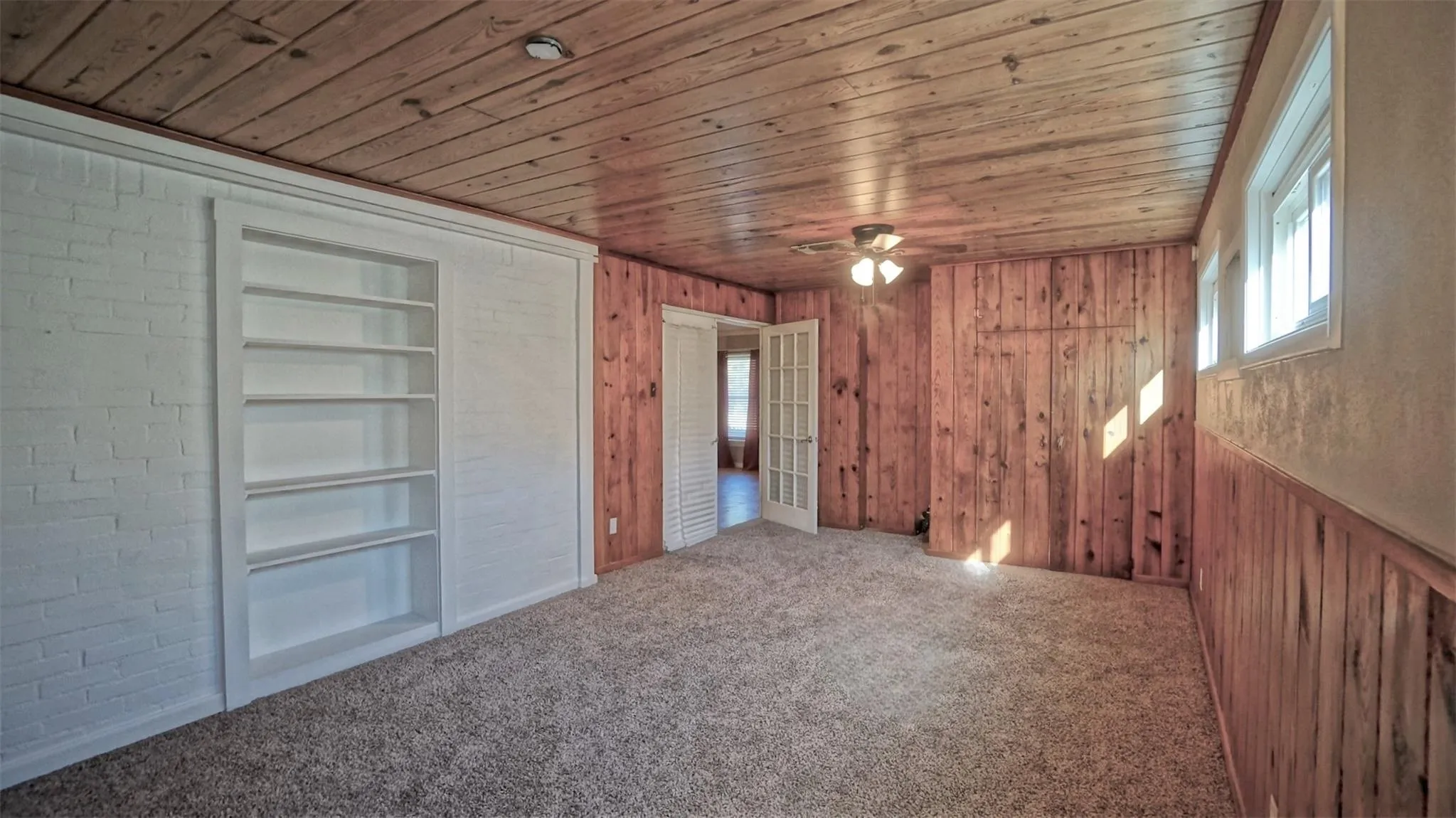 Unfurnished bedroom featuring multiple windows, wooden ceiling, carpet flooring, and wood walls