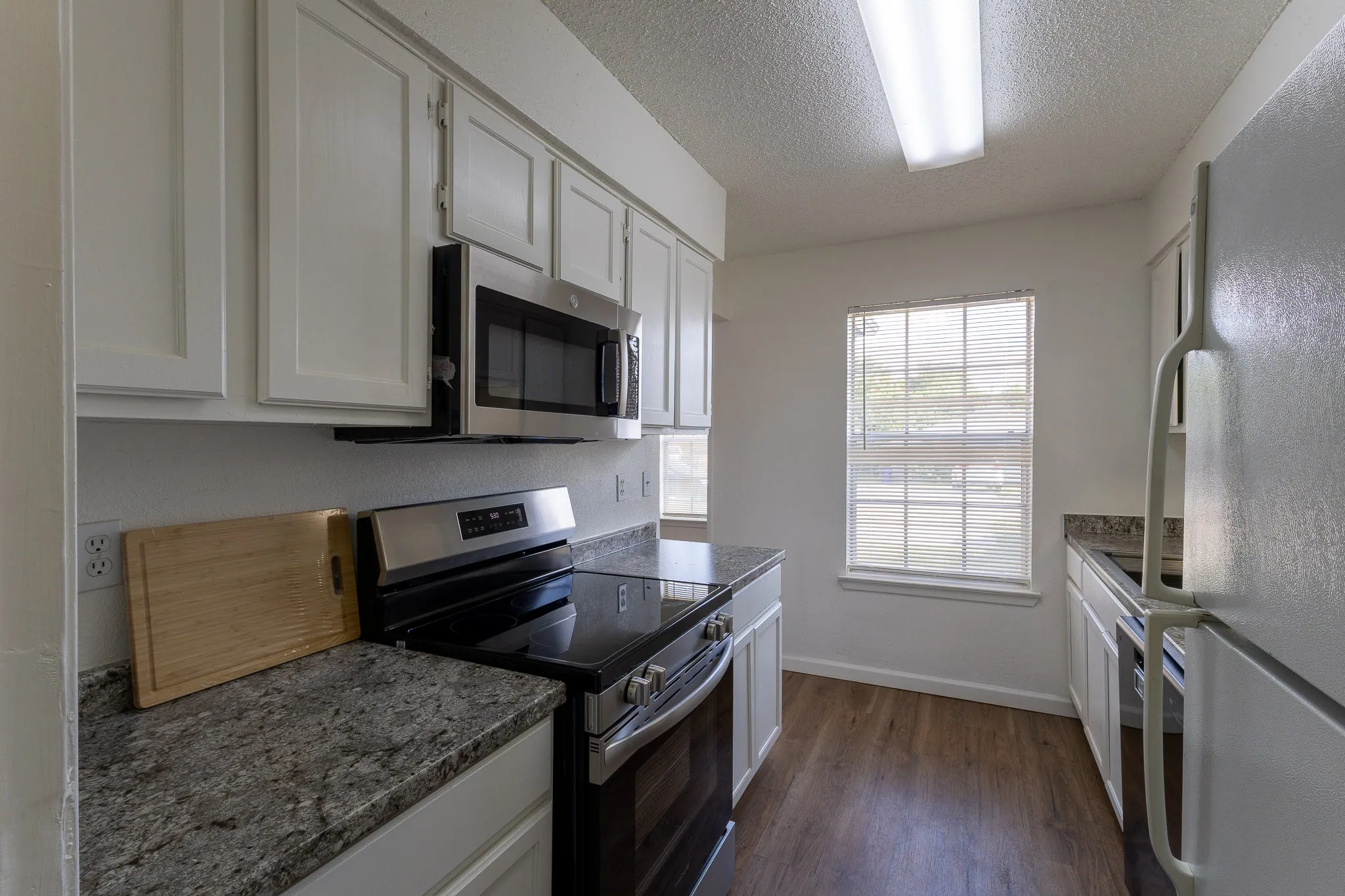 Kitchen featuring white cabinetry, granite-finish countertops, stainless steel appliances, wood-finish flooring, and a window with blinds