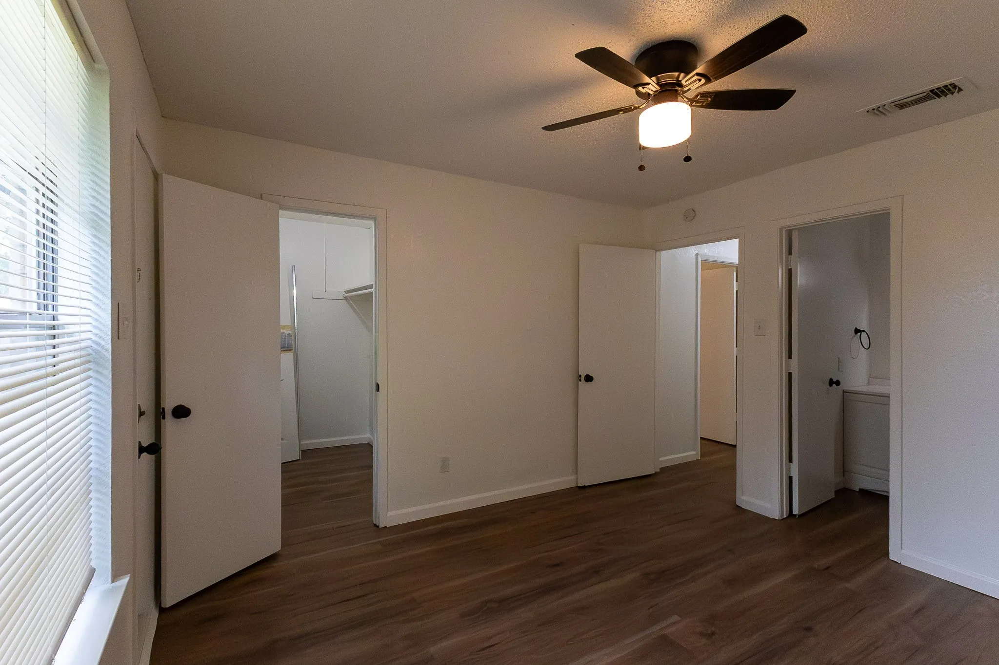 Wood-finish flooring, ceiling fan with integrated lighting, window with blinds, and white interior doors