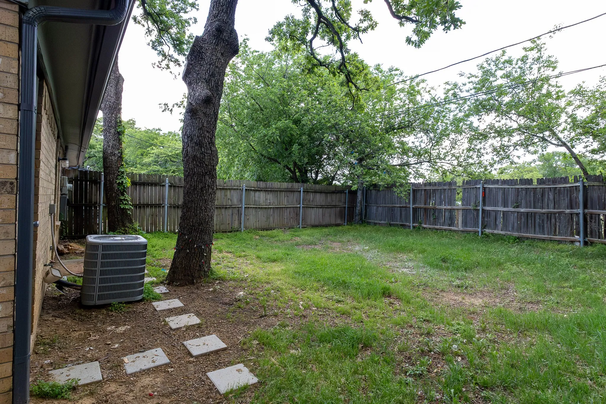 Expansive fenced yard featuring mature trees and a brick exterior