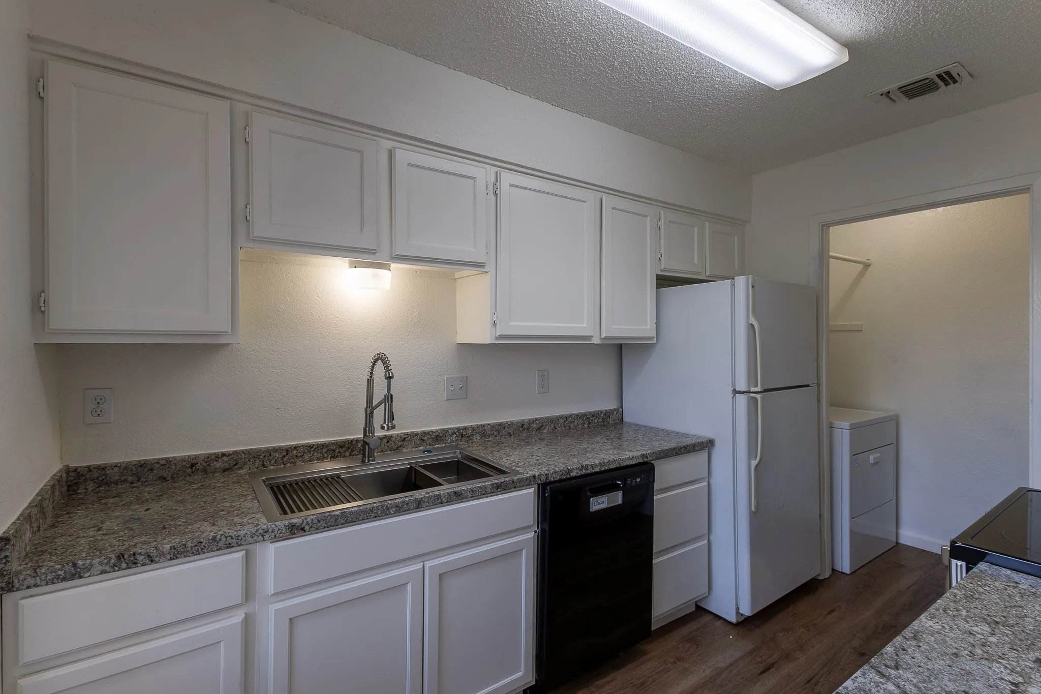 Kitchen featuring white cabinetry, speckled countertops, a stainless steel double sink with a high-arc faucet, and wood-finish flooring