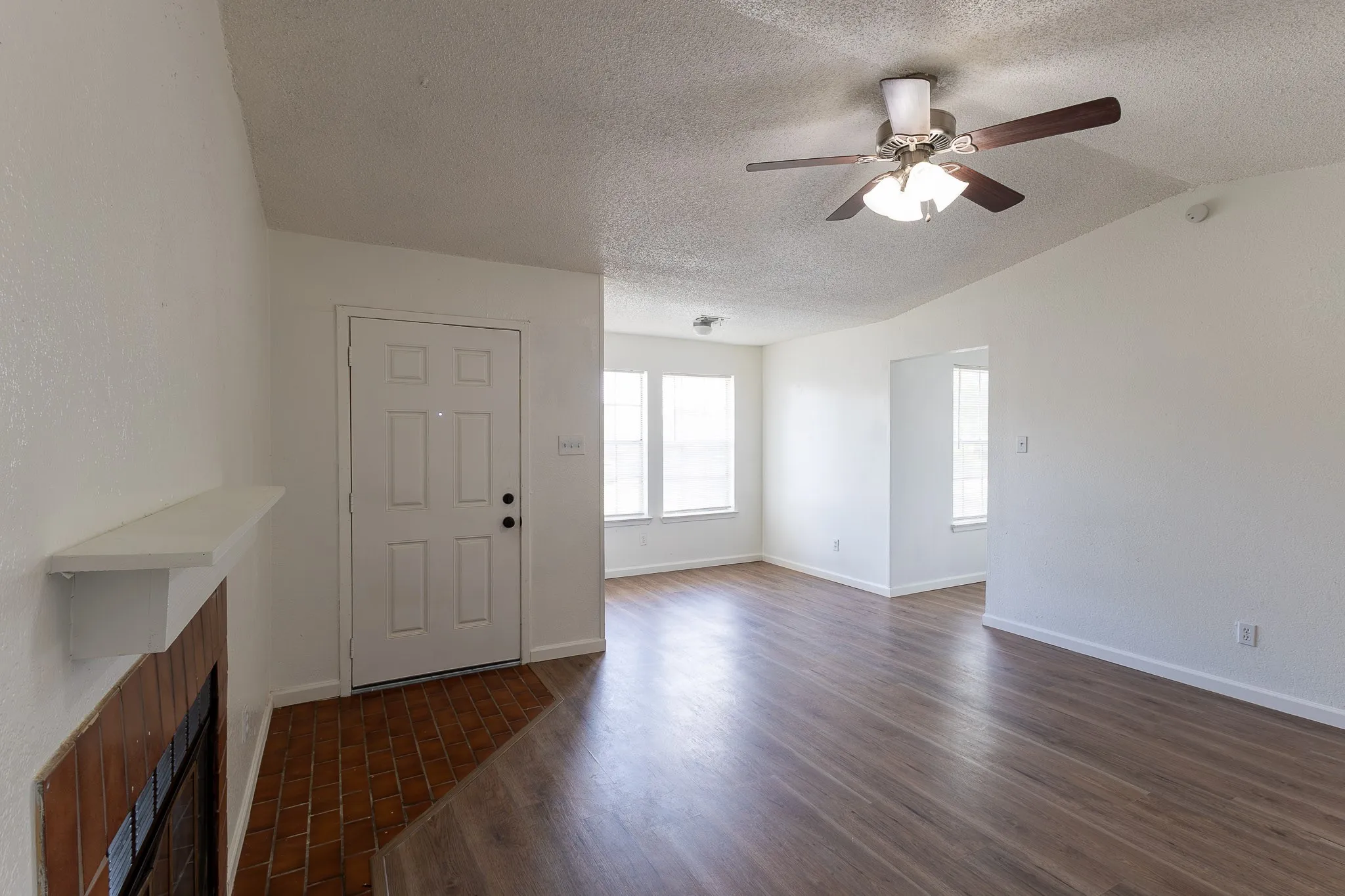 Spacious living area featuring wood-finish flooring, white walls, and a ceiling fan with integrated lighting