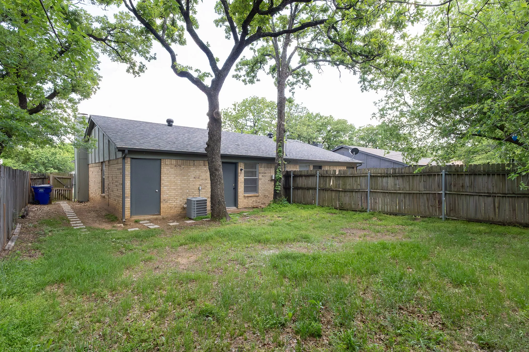 Spacious backyard featuring a wood privacy fence, mature trees, and a brick exterior
