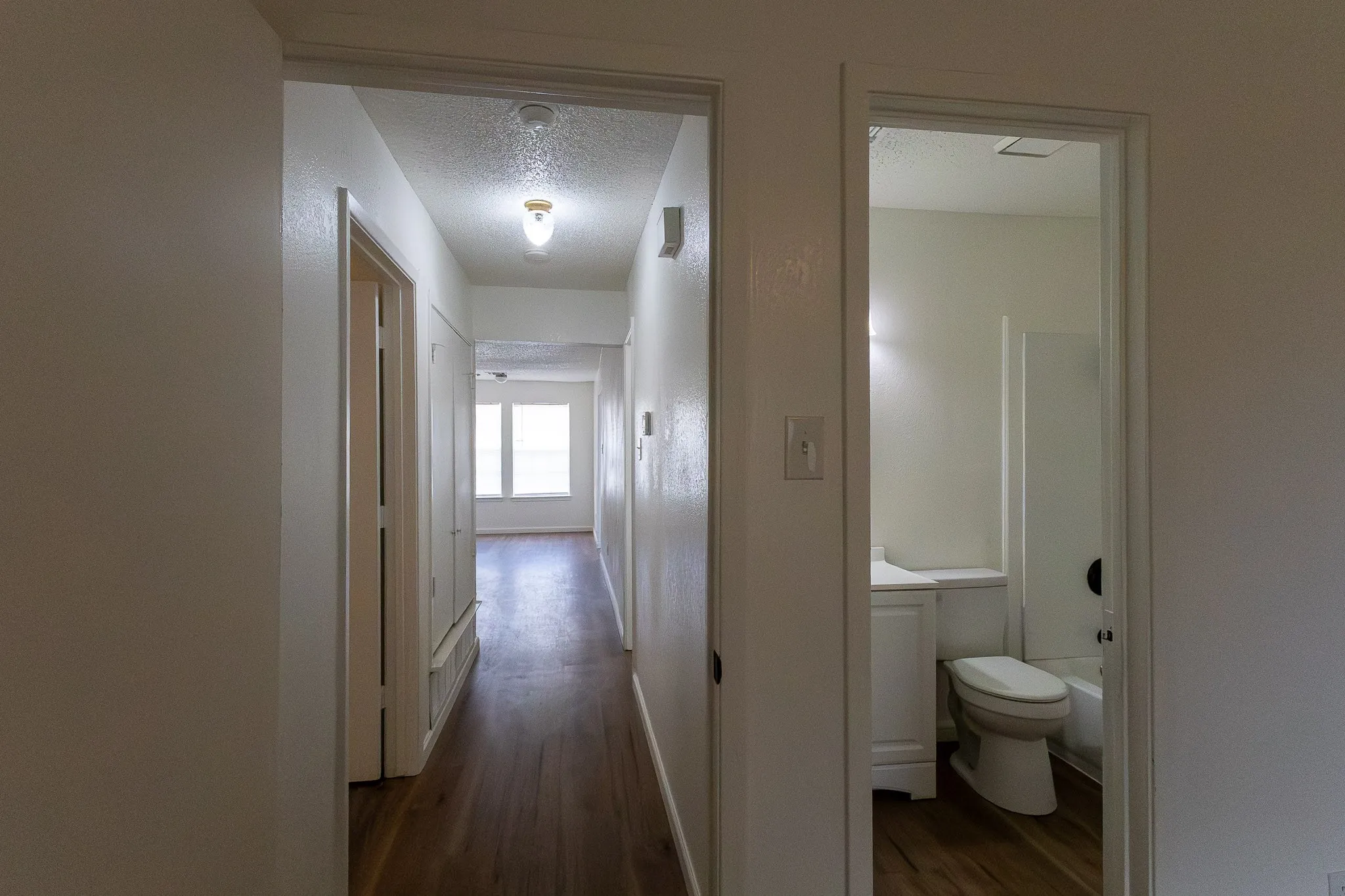 Hard-surface flooring throughout, neutral paint finishes, white paneled doors, and a bathroom featuring a white vanity with integrated sink and a white tub with shower surround