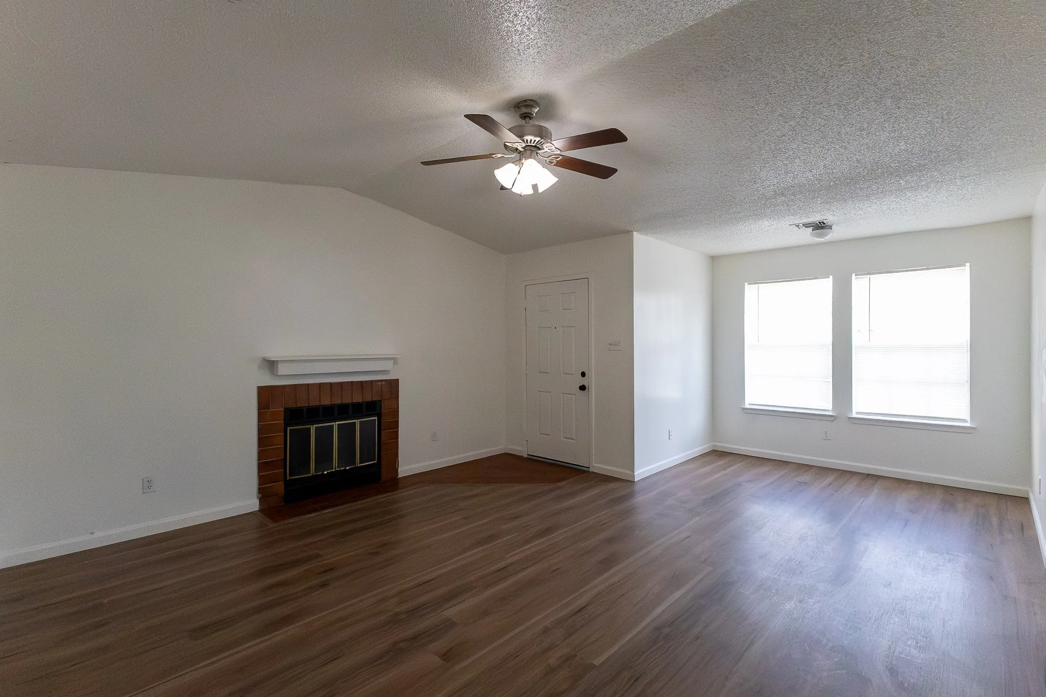 Vaulted ceiling, wood-finish flooring, brick fireplace with mantel, ceiling fan, multiple windows